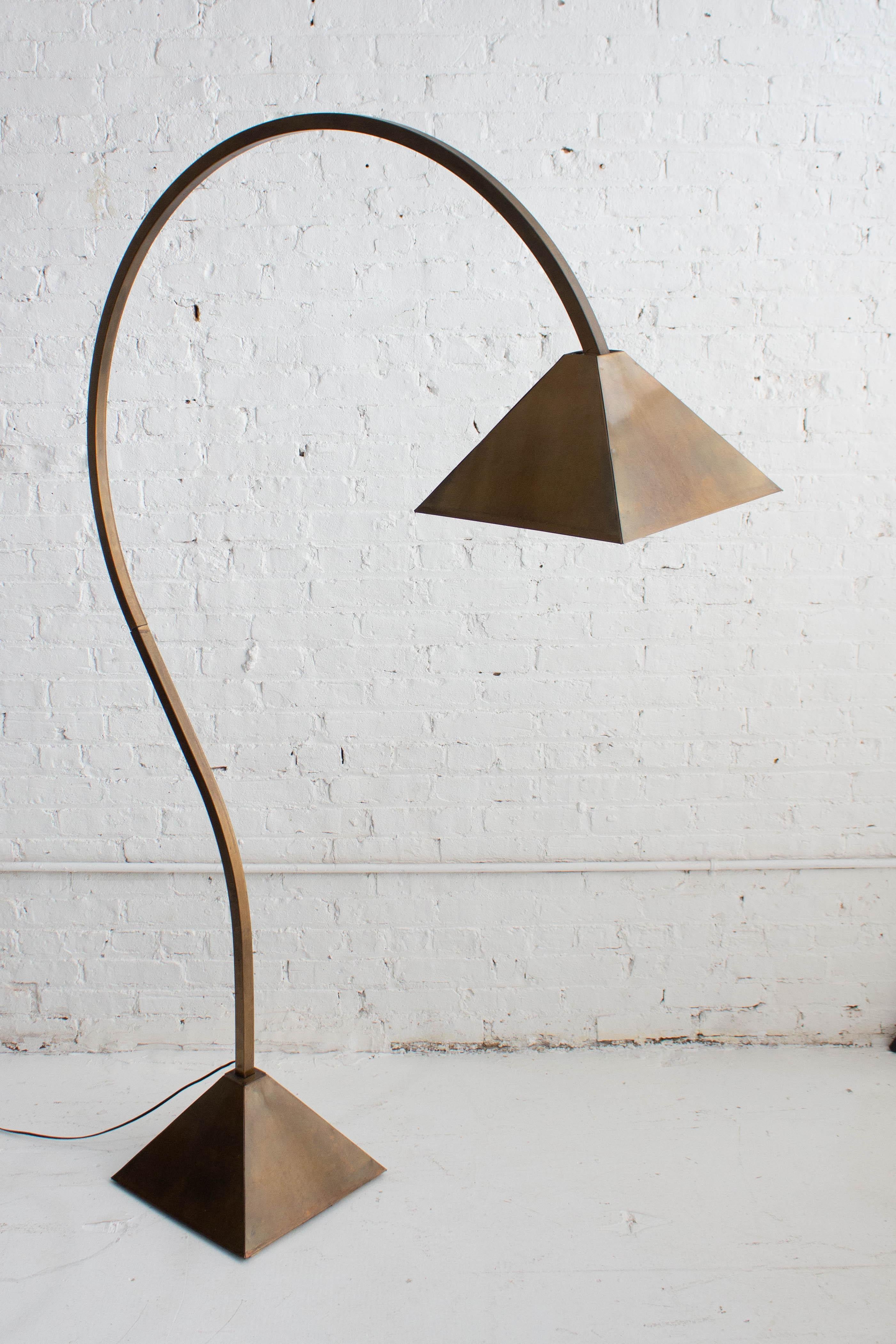 A mid century brass arc floor lamp. Richly burnished brass finish. Angular pyramid base and shade. Evident details of the makers hand can be seen throughout. Base is constructed of a concrete weight to support the arc structure. Sheet brass cap