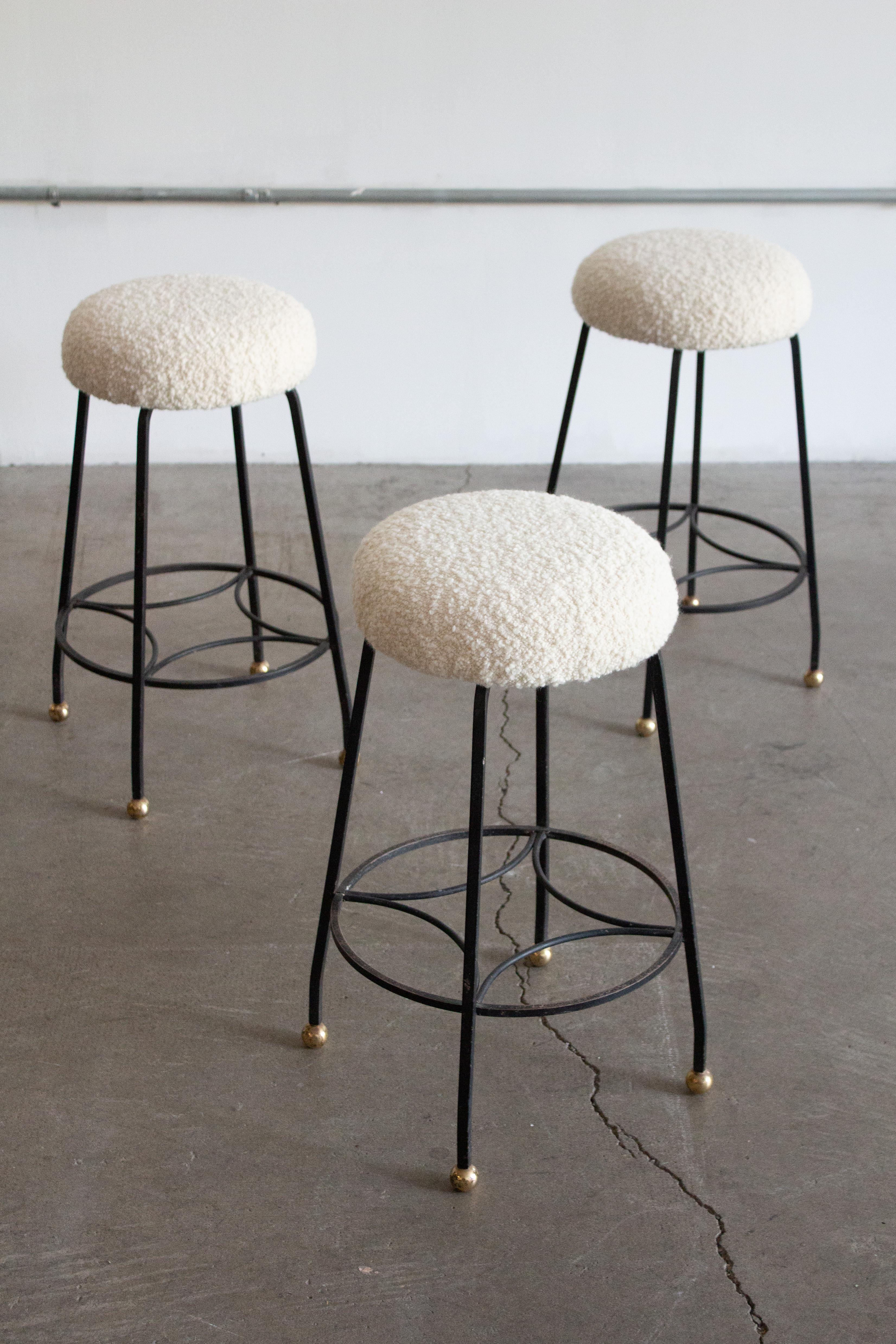 A set of three mid century studio made iron counter stools. New cream bouclé seats and brass ball feet. Patinaed matte back finish to iron frames.