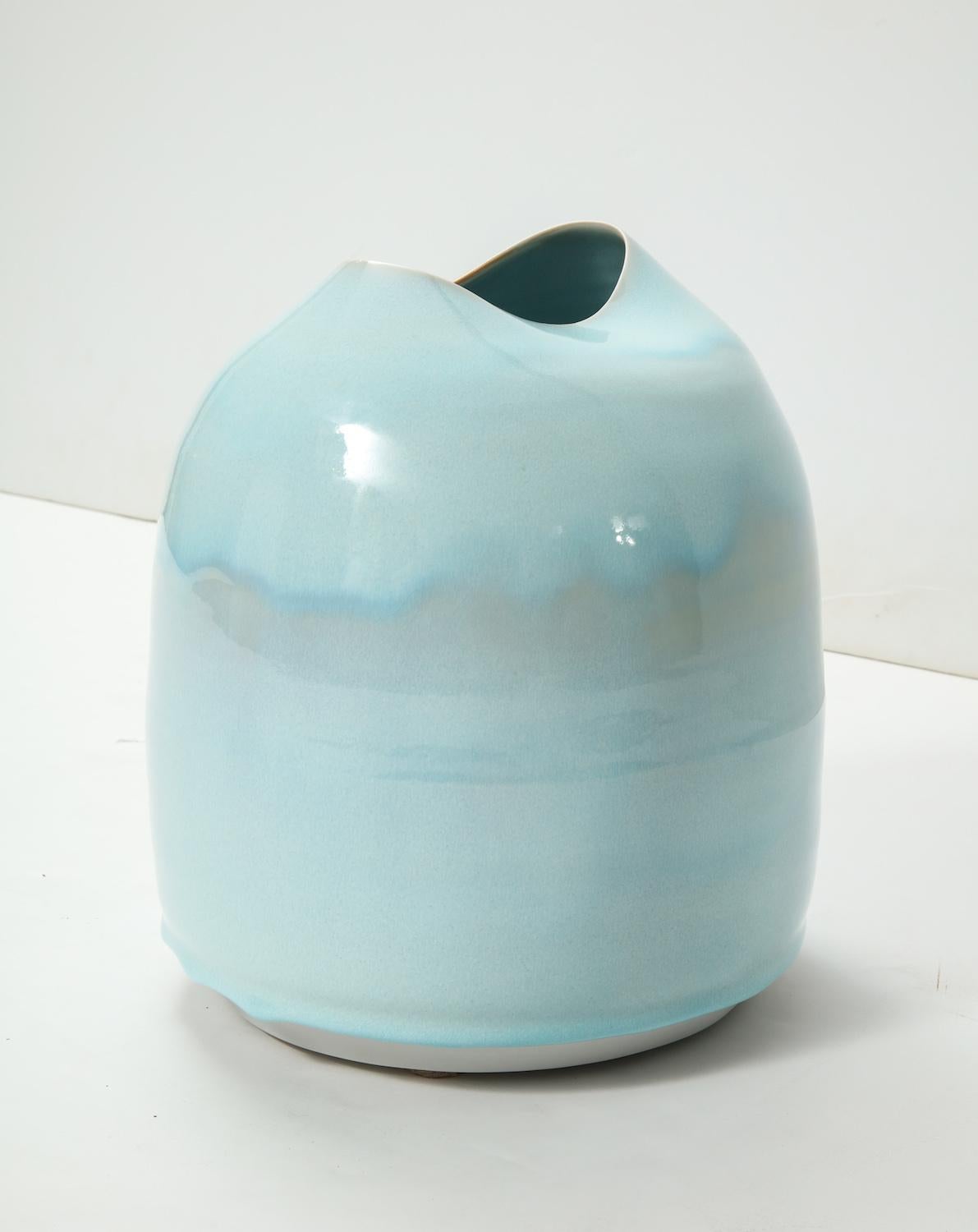 Wheel-thrown porcelain vase with oval formed mouth at top. Pale blue dripping glaze. Signed on underside with artists logo.