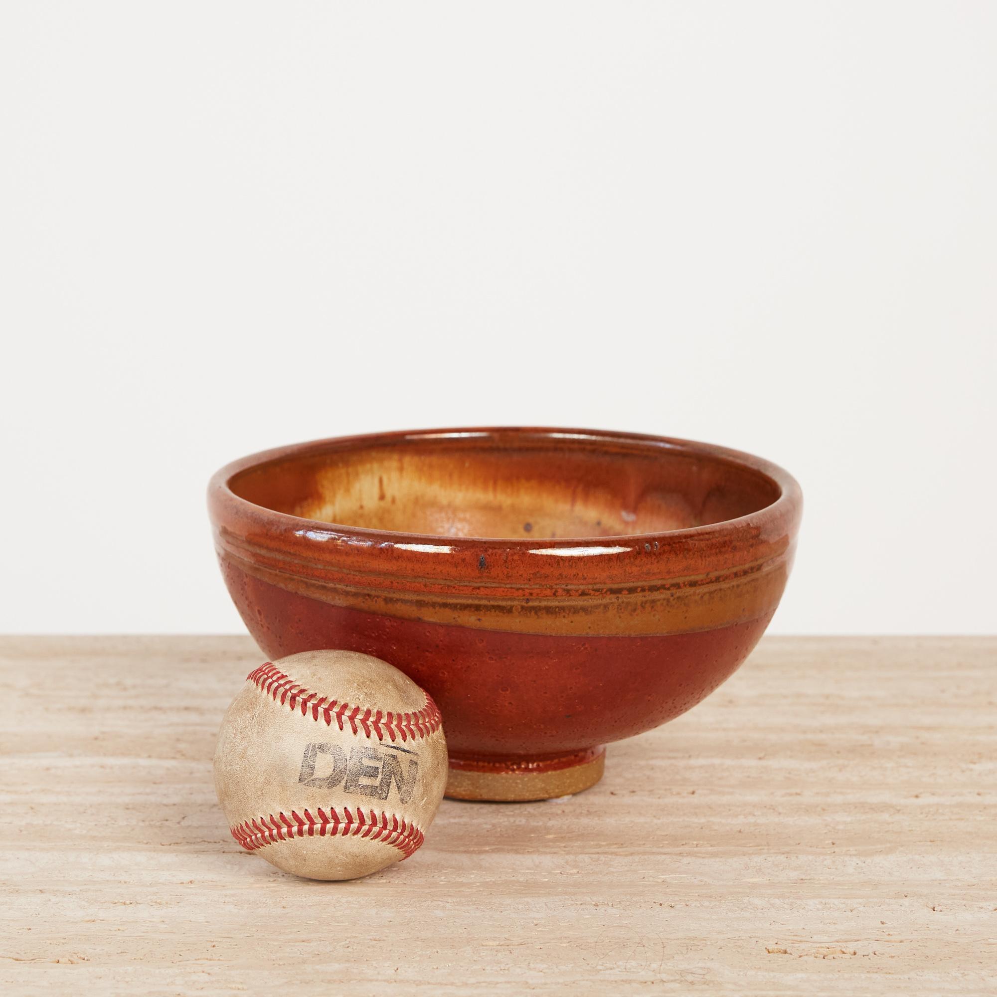 Rust colored footed ceramic bowl. Hand thrown simplicity with textured glaze and soft golden ring along the exterior. The interior features a dramatic gradient with shades of gold, sandstone, and amber with abstract mottle. Bottom features hand