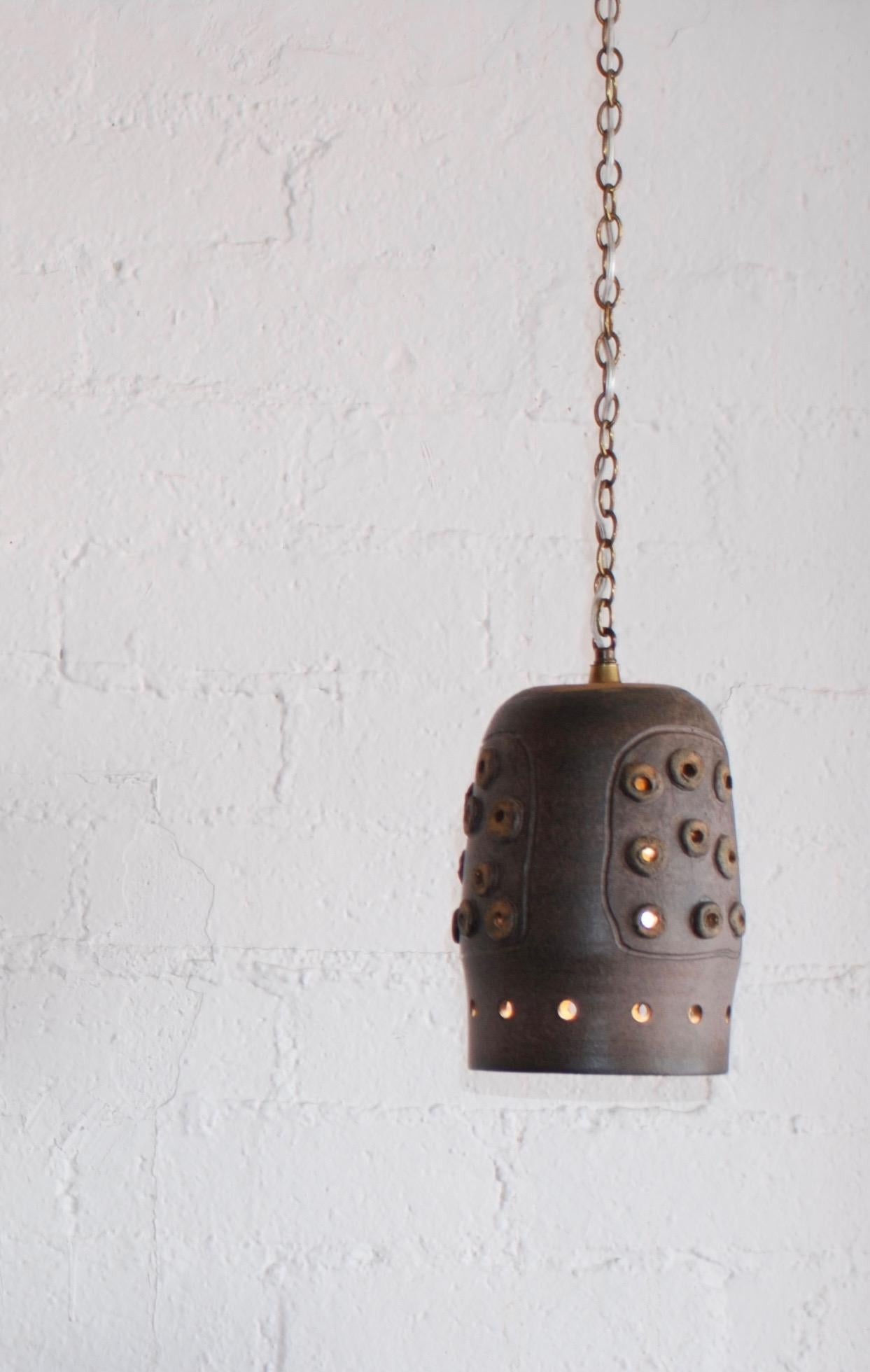 A California Studio Pottery hanging lamp. The pendant has an earth toned glaze and decorative circular penetrations which allows the light to shine through. The pendant is signed although the signature is illegible. The chain is 26