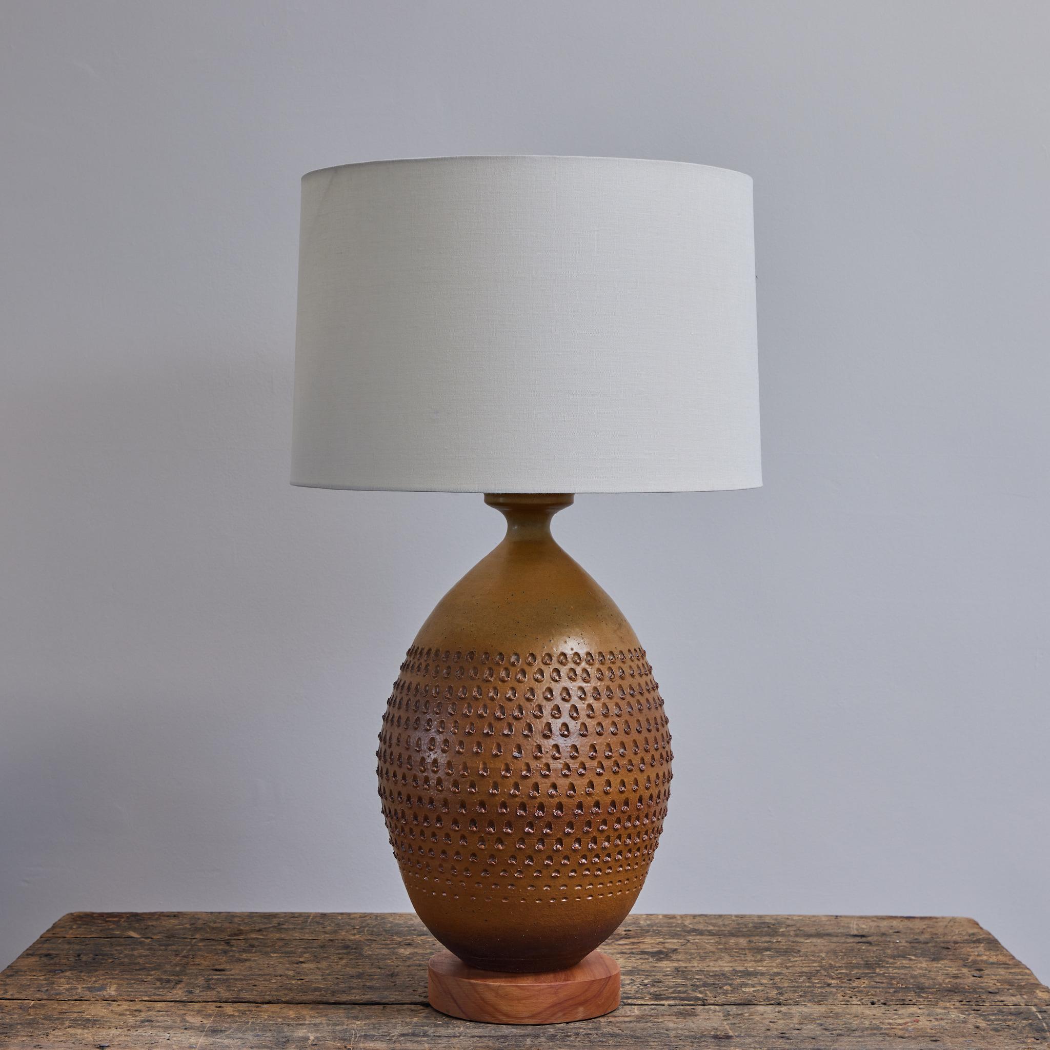 Mid-century modern studio pottery lamp by American ceramicist Roger Bailey. Mounted on a circular wooden base, the ceramic stand is a warm chestnut-auburn, texturally marked by a swath of tightly repeated notches. Swank and organic, the piece