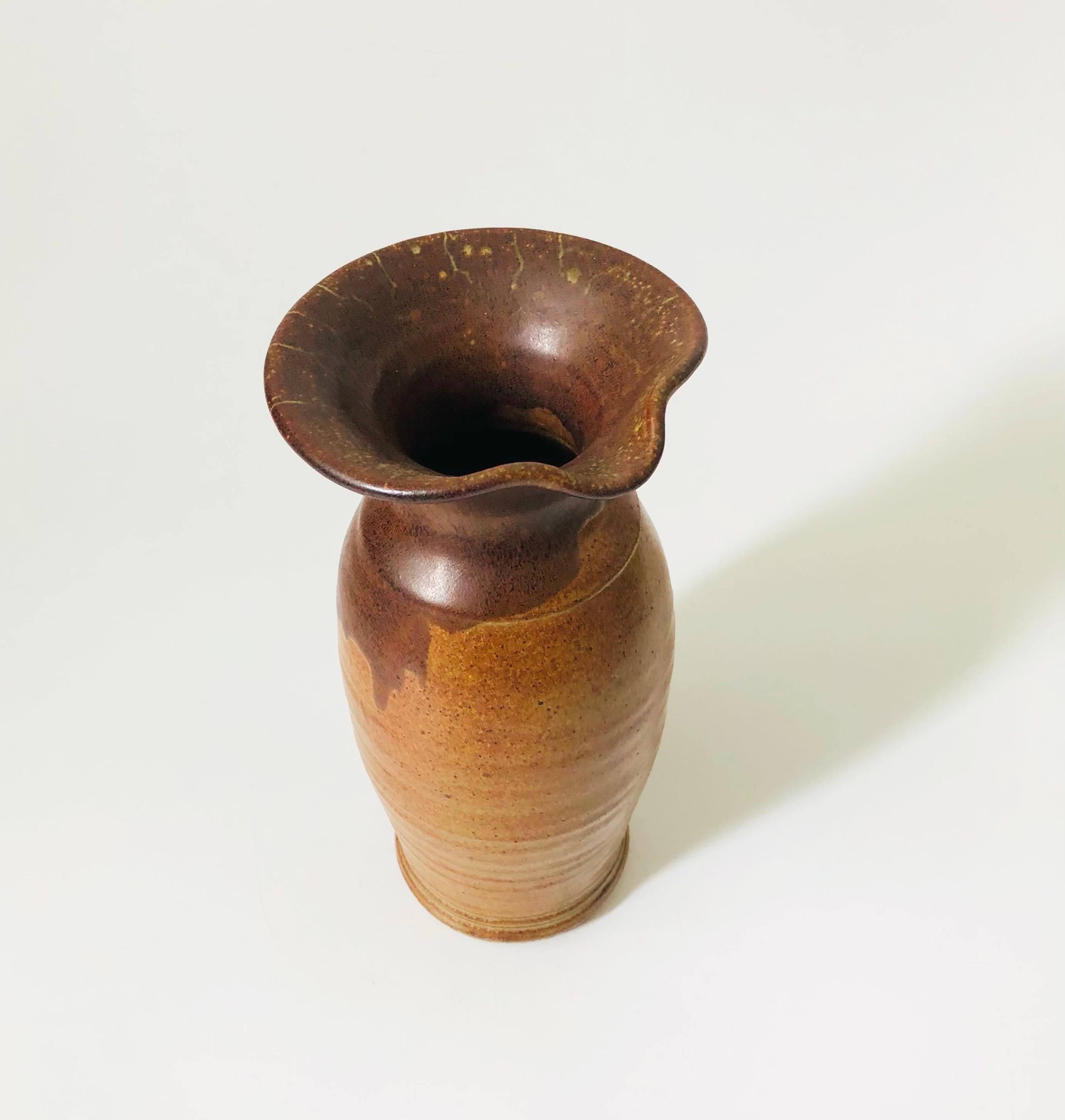 A tall vintage studio pottery pitcher vase. Two tone earthy brown glazes. A spout has been formed on one side of the opening.


