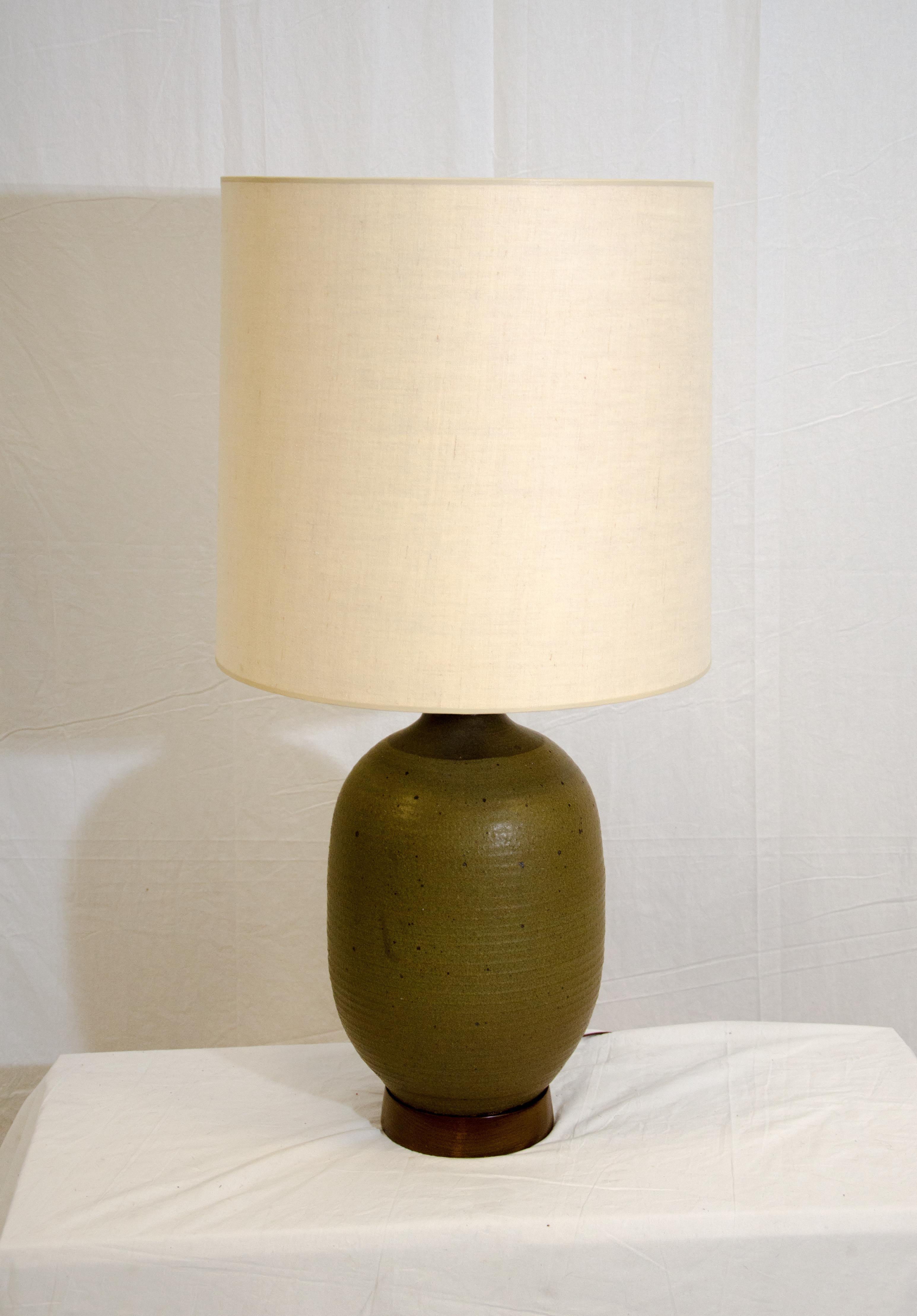 This large Studio Pottery lamp is a muted green color with random darker accent spots and has a ridged design to the whole base. There is a 2