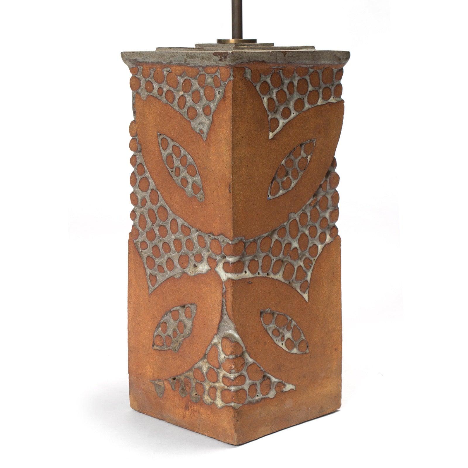 A terracotta table lamp having an impressed foliate pattern with cream glaze highlights.