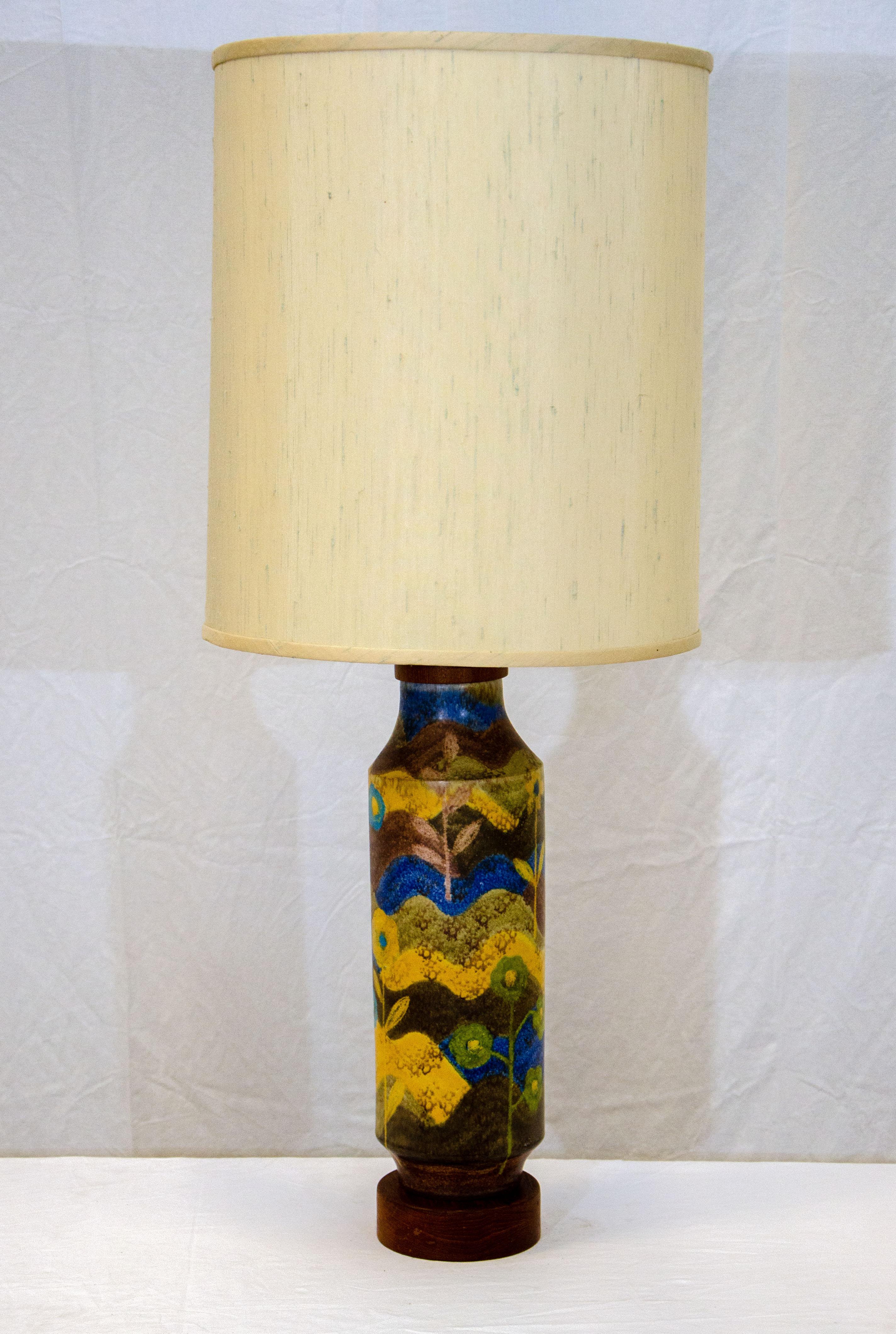 Very nice studio pottery lamp with a walnut base and top, a cylindrical body stylized with a leaf and flower design using alternating colors of blue, green, yellow, brown, and white. The wooden base is 1 3/4