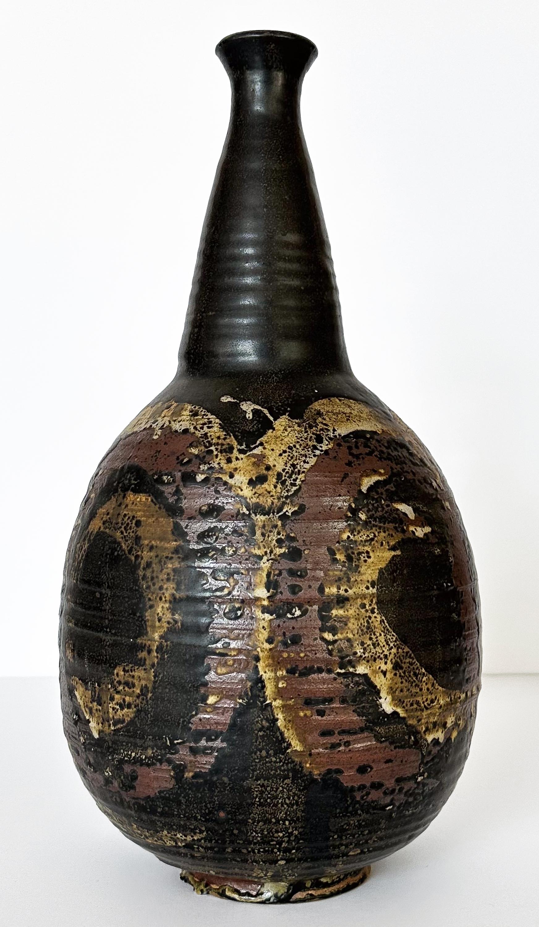 A large studio pottery vase by Laura Vaughn, circa 1960s.  This vase features a dark charcoal background overlaid with brick, tan and ochre glazes in a loose abstract swirling / circular design.  Narrow neck with a 1.75