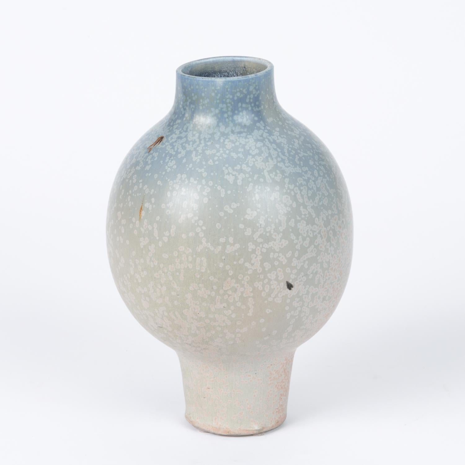 Studio pottery ceramic vase in a beautiful ombre glaze. The pieces features a spherical center form that tapers into a narrow base. The glaze consists of soft blue and light cool gray tones that are accented by contrasting pink and blue speckles