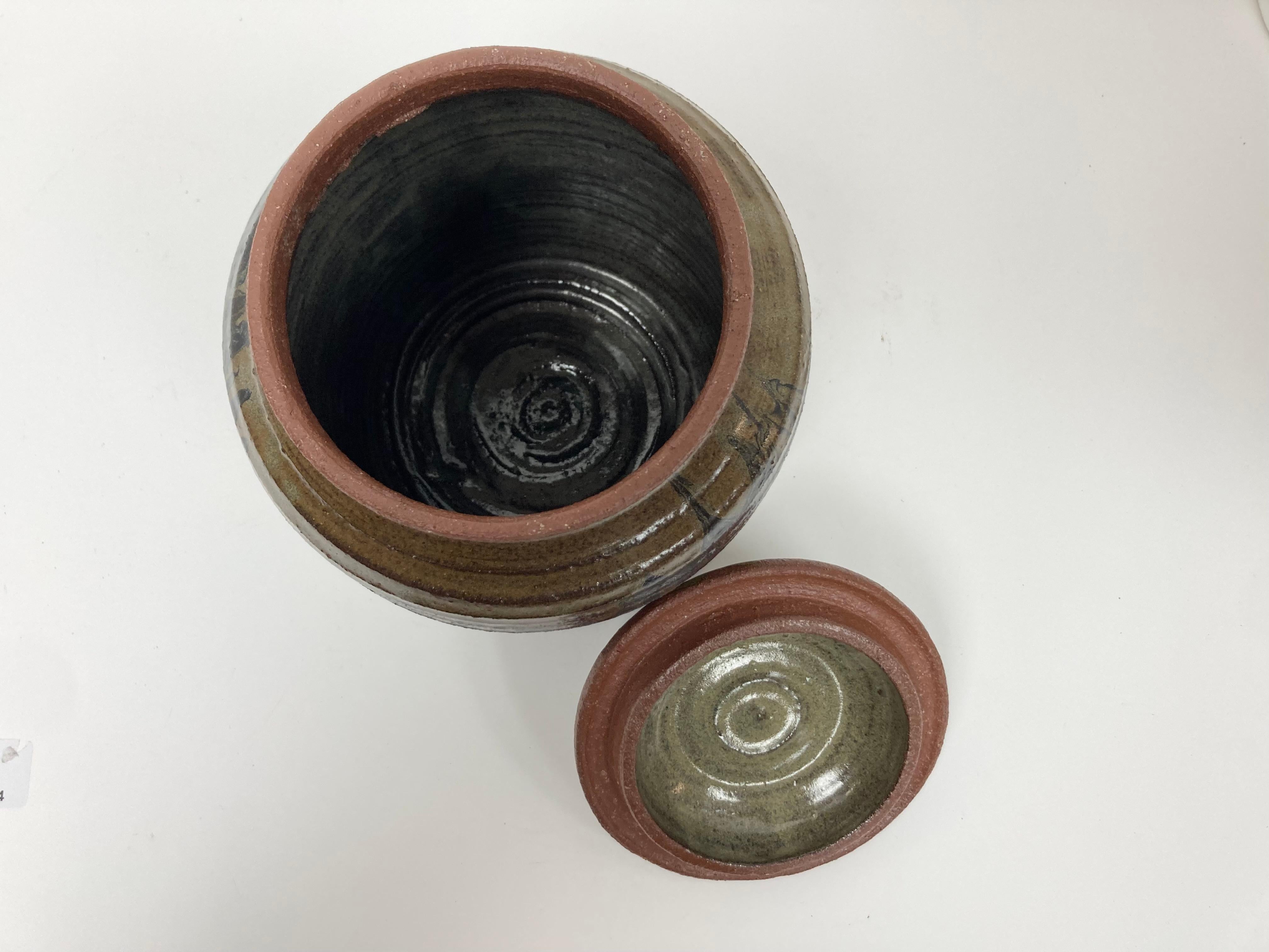 Jarra de agua con tapa, muy bien elaborada, con la forma de los recipientes utilizados en la Ceremonia del Té japonesa. El cuerpo de la jarra está estriado, vidriado y presenta una fina coloración abstracta en un marrón intenso sobre un fondo más
