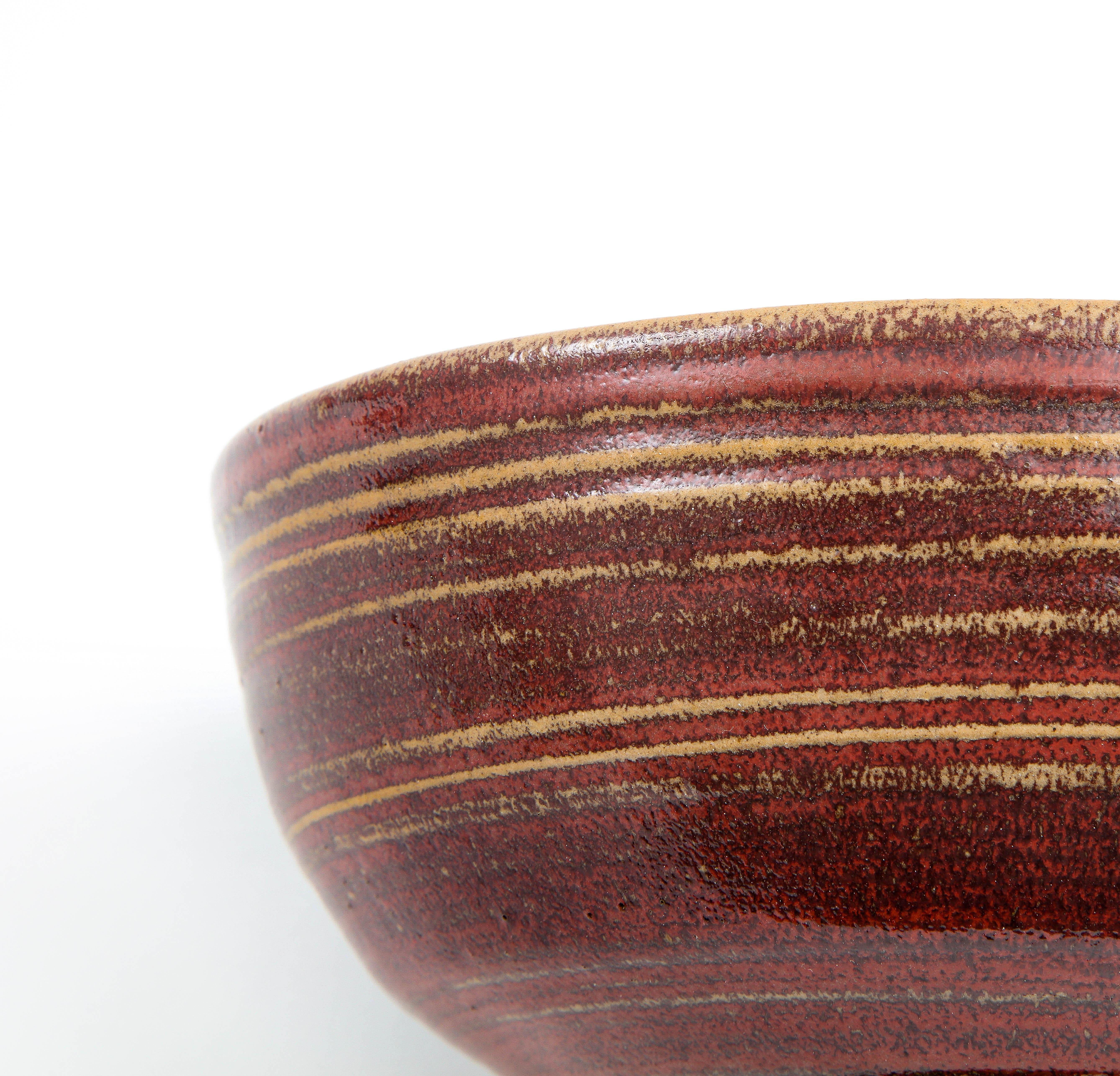 A rustic stoneware bowl on a pedestal. Rich oxblood glaze with hand-drawn lines complementing its simple organic form. The base as little cutouts that lighten the overall structure. Unsigned.