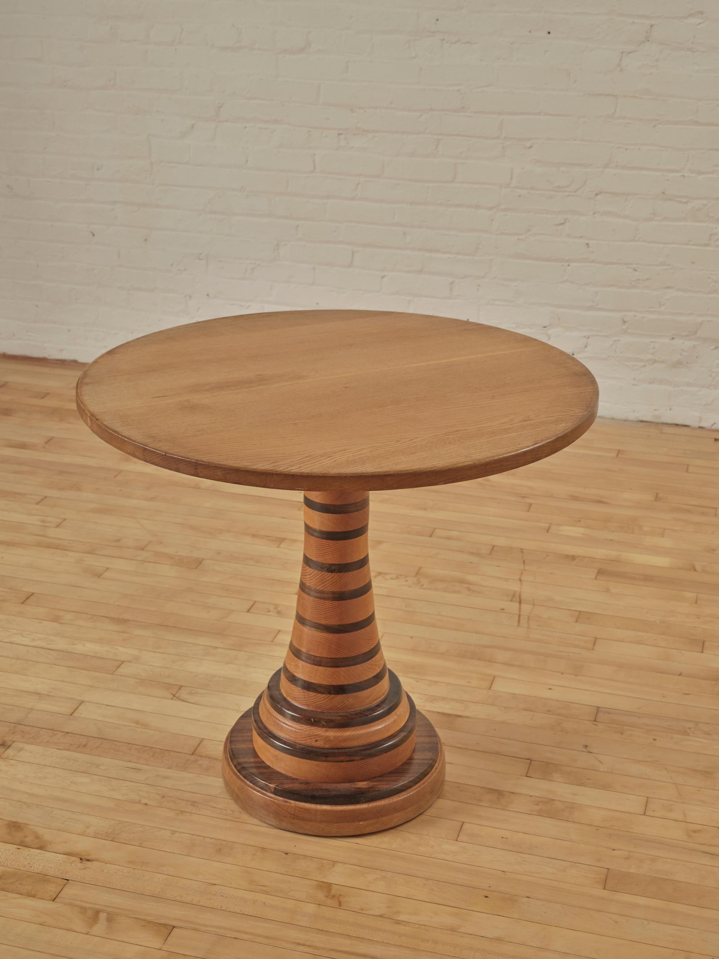 Studio Turned Pedestal Center Table with a striped wooden base. The base is crafted from solid wood, ensuring stability and strength. The circular tabletop maximizes the usable surface area. Whether you're placing it in the center of your living