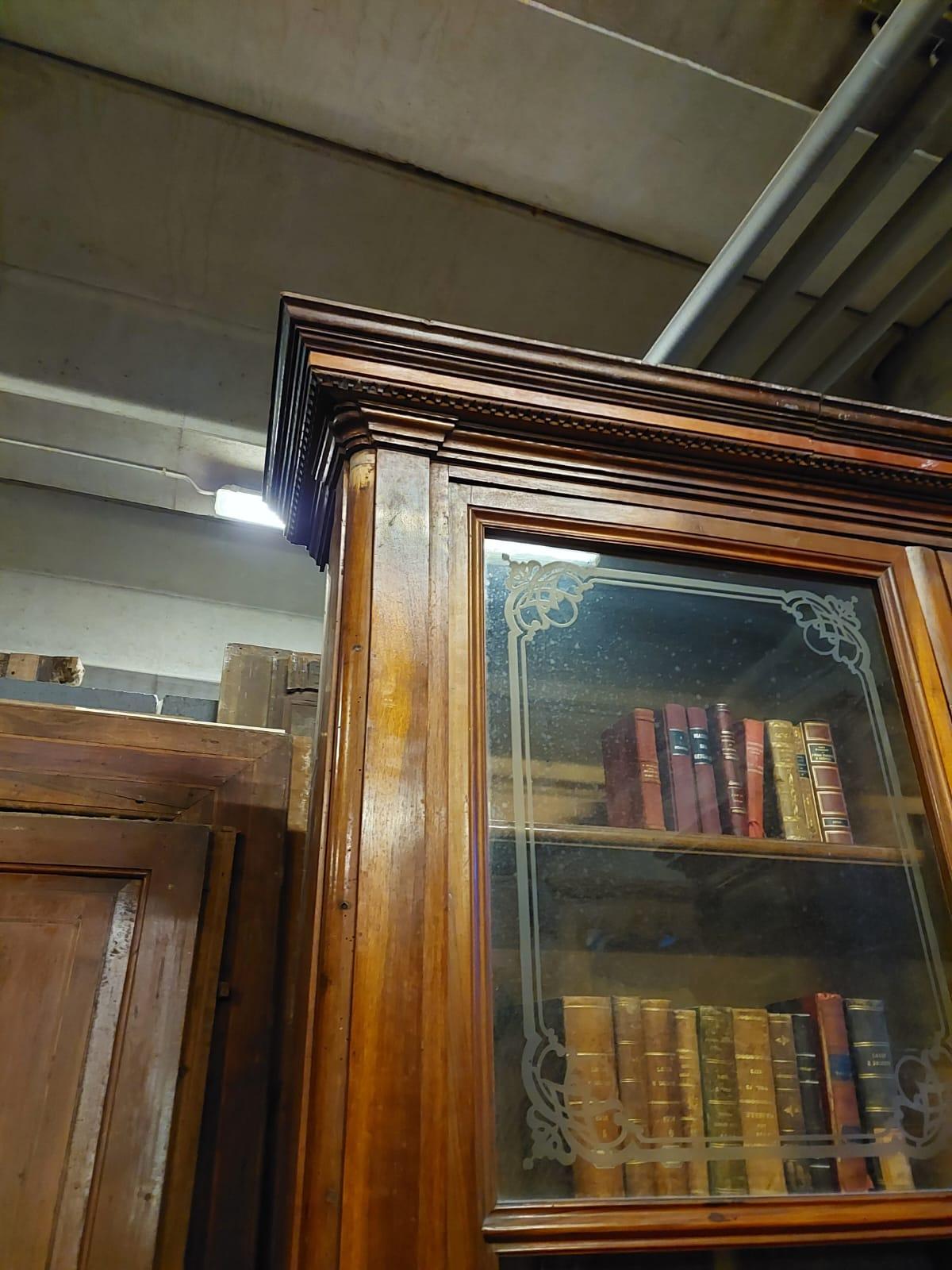 Antica libreria studio, libreria in legno massello di noce, completa di vetri serigrafati, La parte inferiore del mobile ha quattro ante in legno, mentre la parte superiore ha due grandi ante con vetri decorati con motivi dell'epoca, originale del