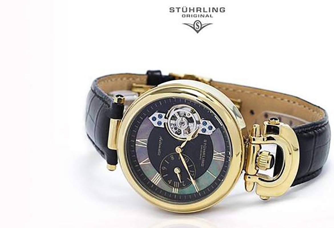 Polished 23K yellow gold layered round shaped case with crown at 12 o'clock position^Protective Krysterna crystals on front and back^Black dial with Mother of Pearl inlay and dual time display with open heart exposed movement^Black alligator