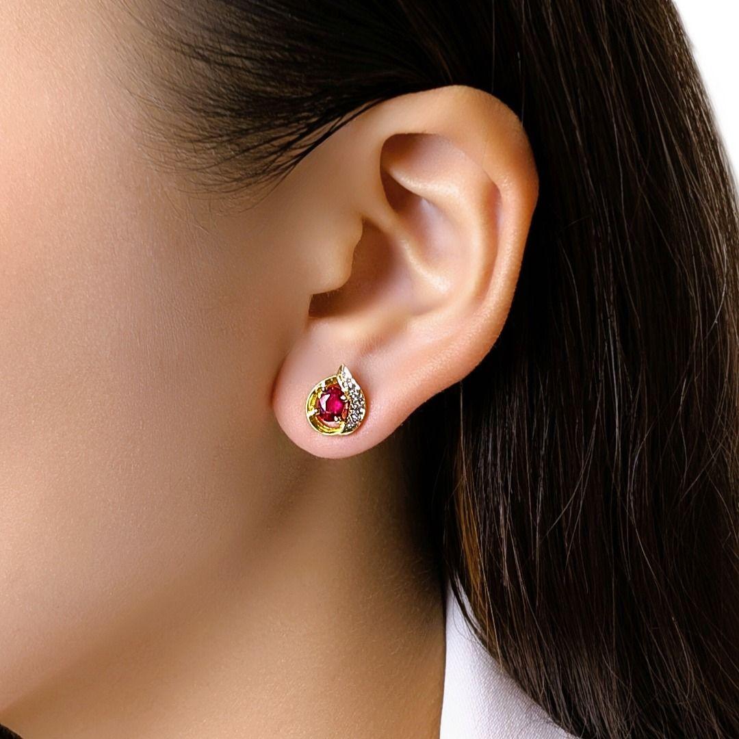 Ces boucles d'oreilles radieuses présentent deux rubis de taille ovale (0,4 ct au total) d'une riche teinte rouge, encadrés par 8 diamants ronds de taille brillante (0,06 ct), de couleur H et de pureté VS, sertis le long d'une gracieuse courbe en