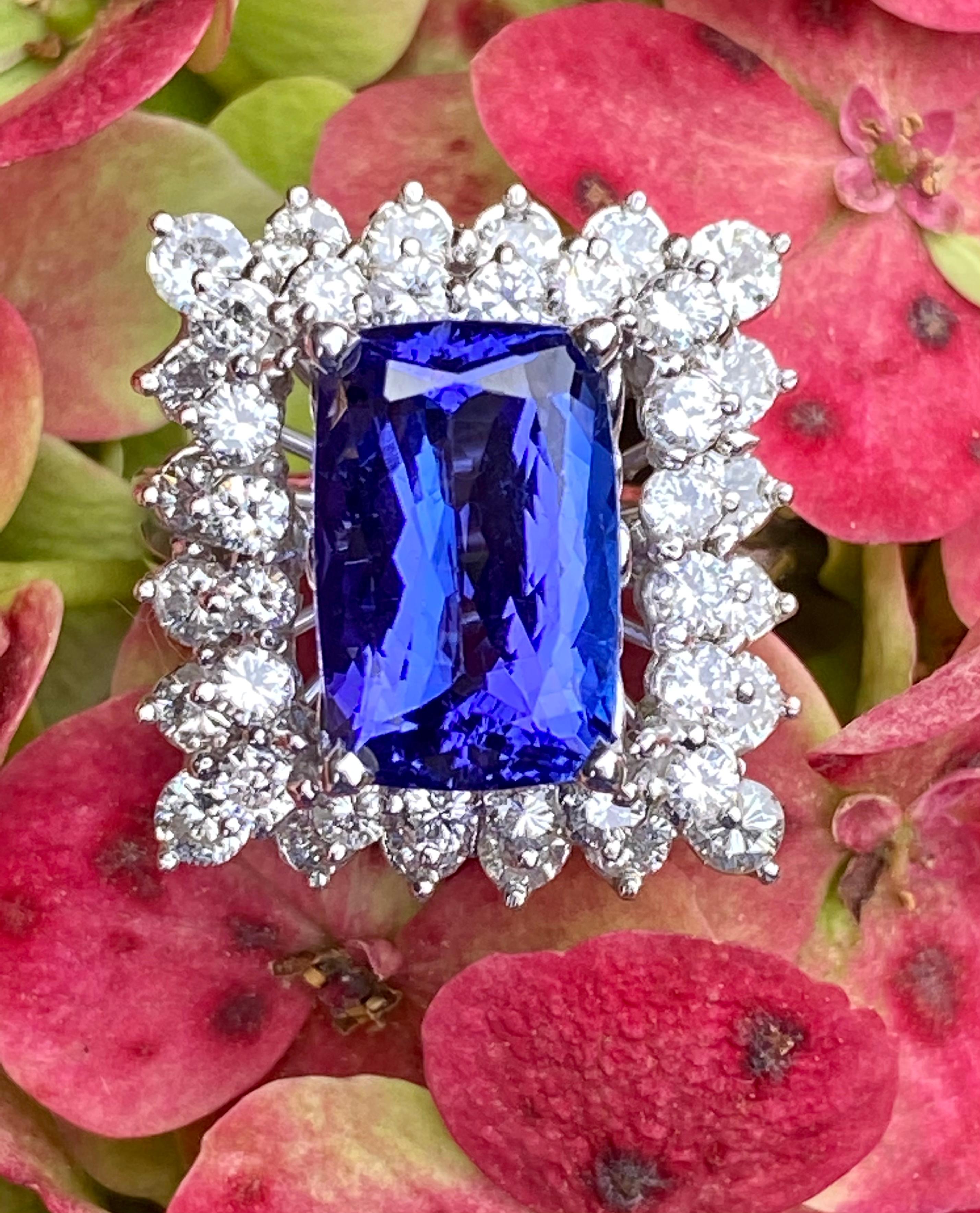 Very elegant and showy, 14 karat white gold cocktail ring features a large, rectangular radiant cut, prong set vivid tanzanite, surrounded by a pair of stepped down round brilliant, prong set diamond halos.  The tanzanite is the most beautiful deep