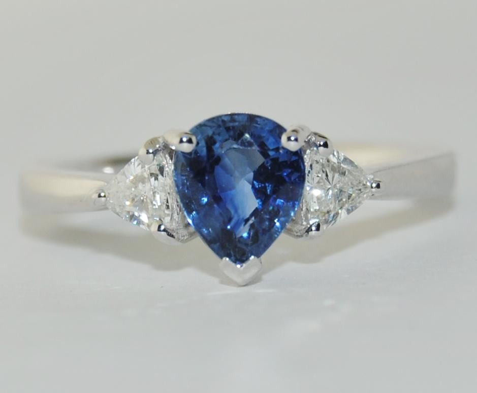 Pear shape 1.22 Carat Blue Sapphire Ring with 2 Triangular Brilliant White Diamonds 0.35 Carat on the side.  This new ring is made of 18 Karat White Gold.  Size 6.75