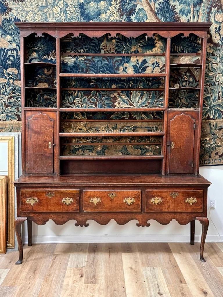 18th Century English Welsh dresser, from an estate in Yorkshire. Having exceptional patina, the open rack with molded cornice and outset side shelves above shaped hinged side cupboards; the base with three drawers fitted pierced brass handles above
