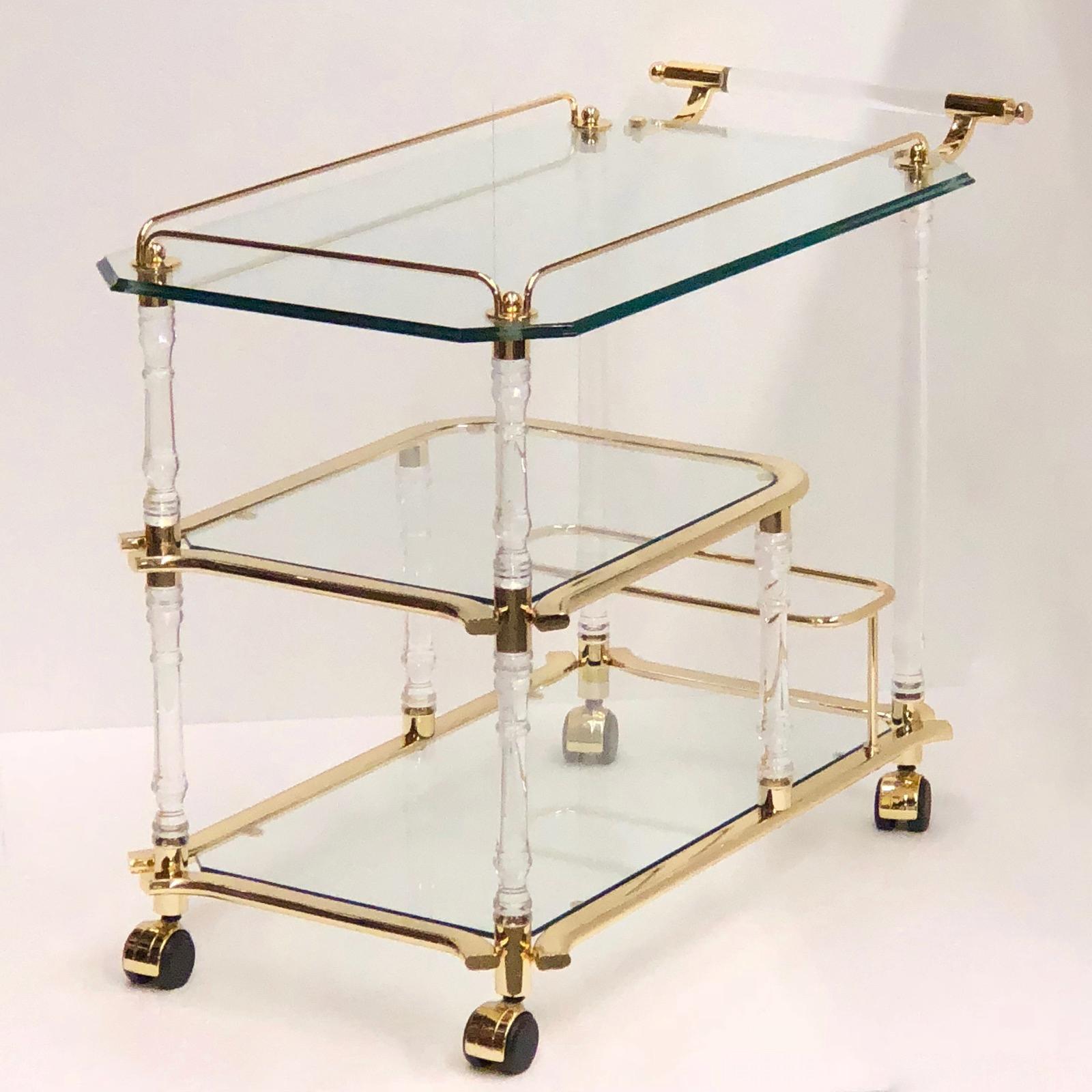 Offered is an absolutely stunning, 1980s bar cart, tea trolley or drinks stand. Three heavy glass plates, four Lucite columns, a Lucite handle and a gold plated frame gives this piece a classy statement. A nice addition to every room or a patio.