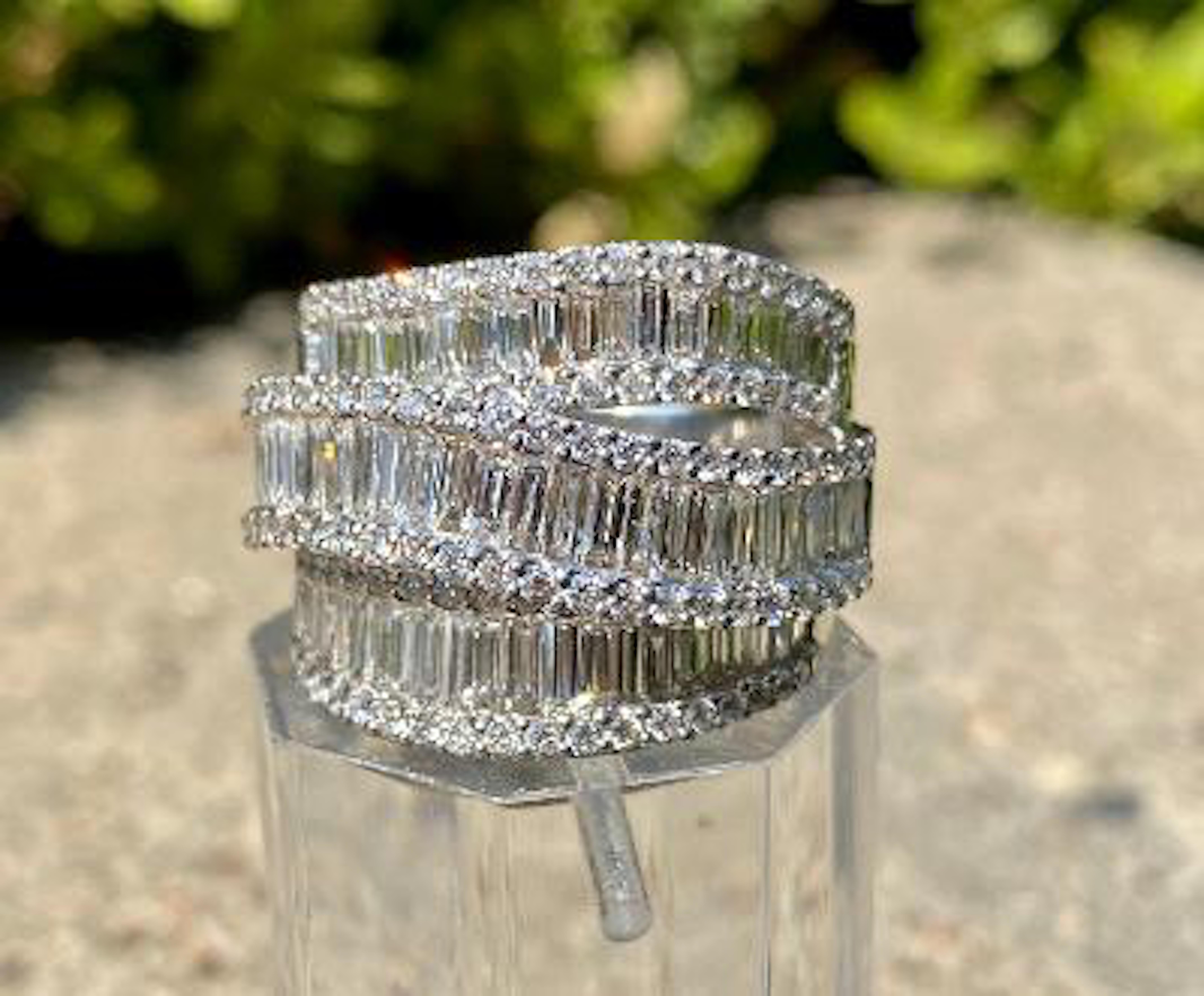 Very elegant and stunning, custom made 14 karat white gold, wide three row band ring features individual rows of sparkling white baguette cut diamonds invisibly set and separated by raised curving lines of prong set round brilliant diamonds creating