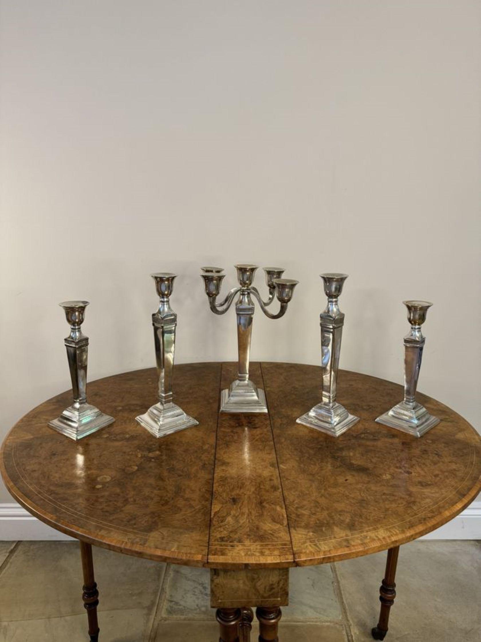 Un completo di cinque candelieri in argento placcato di qualità, composto da un candelabro centrale e due coppie di candelieri graduati che lo accompagnano, sollevati su basi quadrate.

Candelabro H37cm L23cm P23cm
Candelieri medi H36cm L12cm