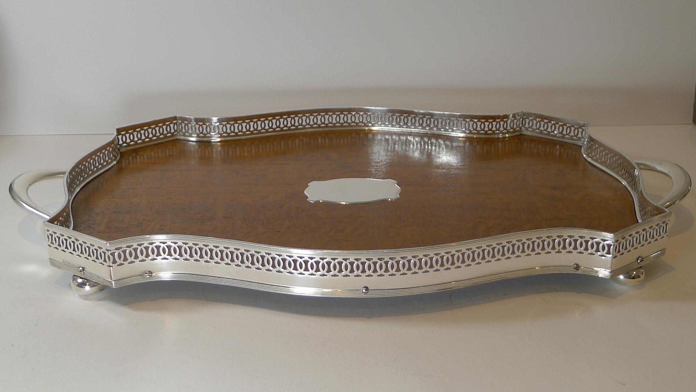 A beautiful antique English drinks / cocktail tray dating to c.1900, late Victorian or early Edwardian.

The shaped tray stands on four bun feet, has two elegant handles and a central vacant cartouche mounted to the centre of the Oak base.

The