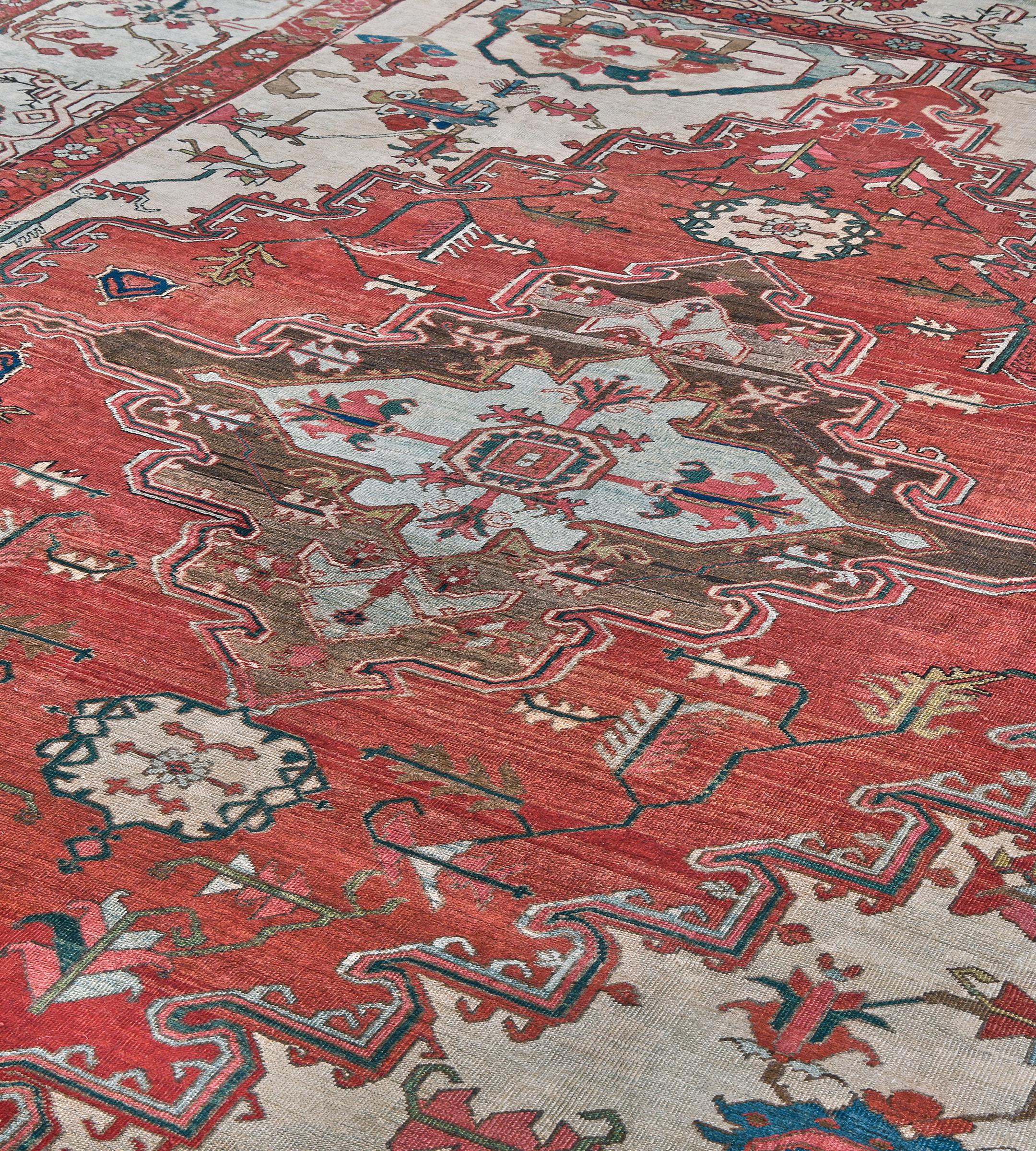 This traditional hand-woven Persian Serapi rug has a brilliant shaded ruby field of sparse angled palmette and tendril vines, enclosing a shaded java brown meandering lozenge medallion, in a shaded ivory and pastel blue sparse meandering palmette