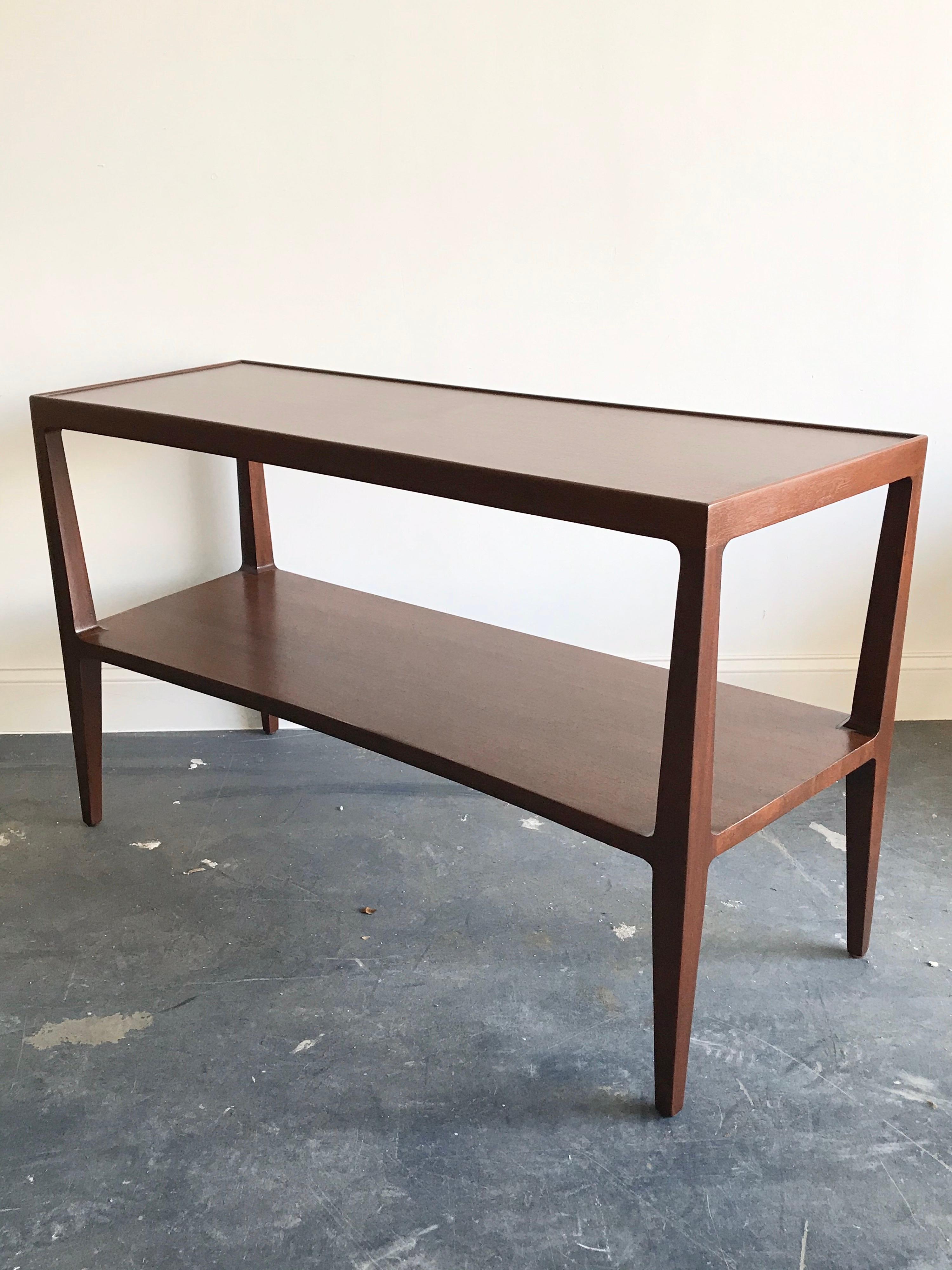 Restored console table designed by Edward Wormley for Dunbar. Features a two-tier design done in mahogany. A soft lip follows the outline of the top shelf, with sculpted legs, angled ends, and graceful curved front. Relatively uncommon