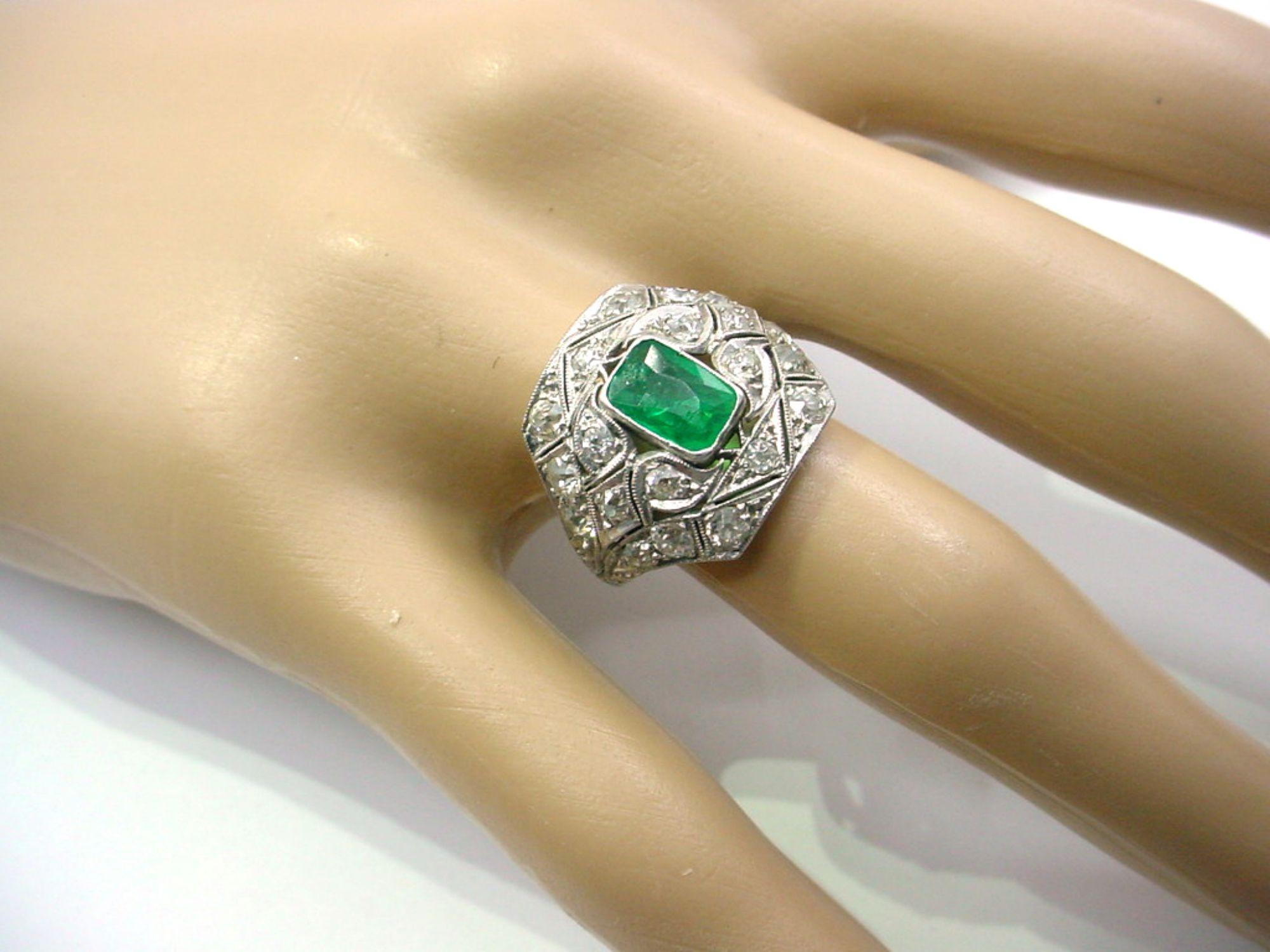 Stunning authentic Art Deco ring rendered n luxurious platinum...    The ornately engraved and openwork mounting, featuring leaves and vines, enhanced with 20 old cut diamonds approx. 1.24 cts.  Ring size 5.5 US and sizeable.  

The central emerald