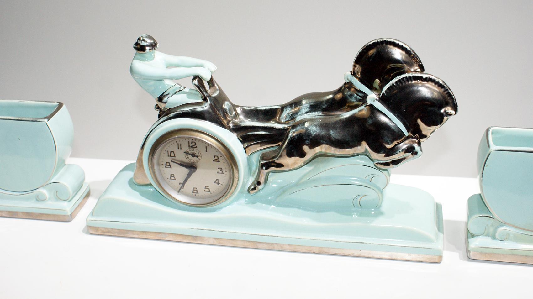 Art Deco mantel ornament clock. A piece depicting the famous gladiator “Ben Hur” in his horse chariot with two rearing horses and two key bowls.
Made in enamel ceramic with light green and gilt colors.
The bowls are numbered: 51.
Dimensions of