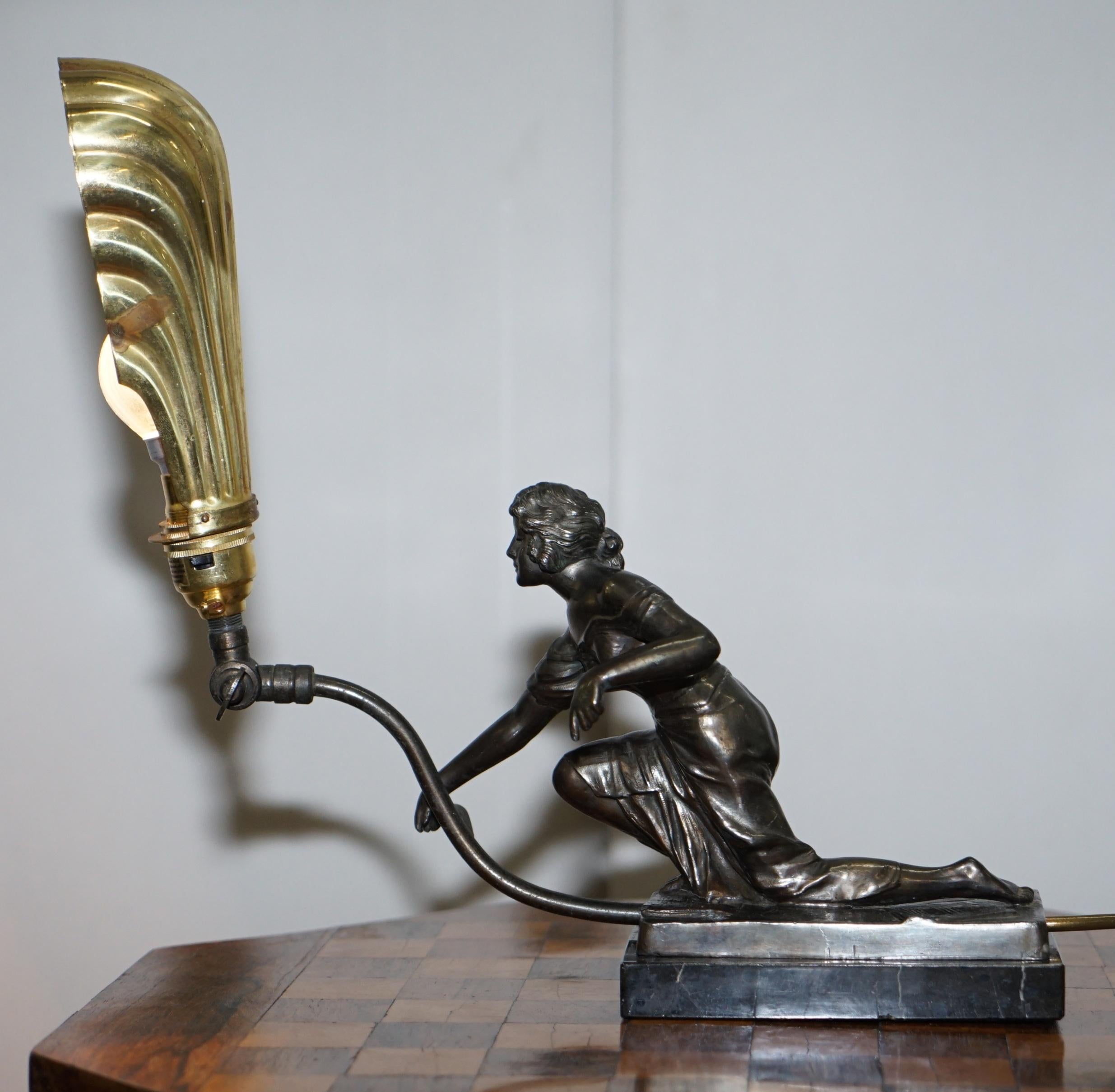 Nous avons le plaisir de proposer à la vente cette belle lampe de table Art Déco originale avec base en marbre, statue en bronze et abat-jour en coquille en bronze doré.

Cette lampe décorative de belle facture est dotée d'un abat-jour articulé et