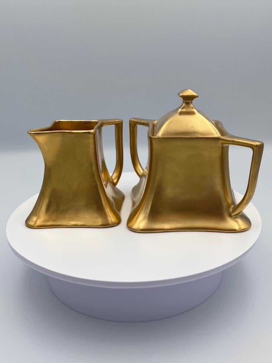 Este juego de azucarero y cremera de porcelana de Viena Austria es un impresionante ejemplo de la artesanía europea de principios del siglo XX. Elegantemente acabado en un llamativo dorado metálico, el diseño resalta las gráciles curvas del Art