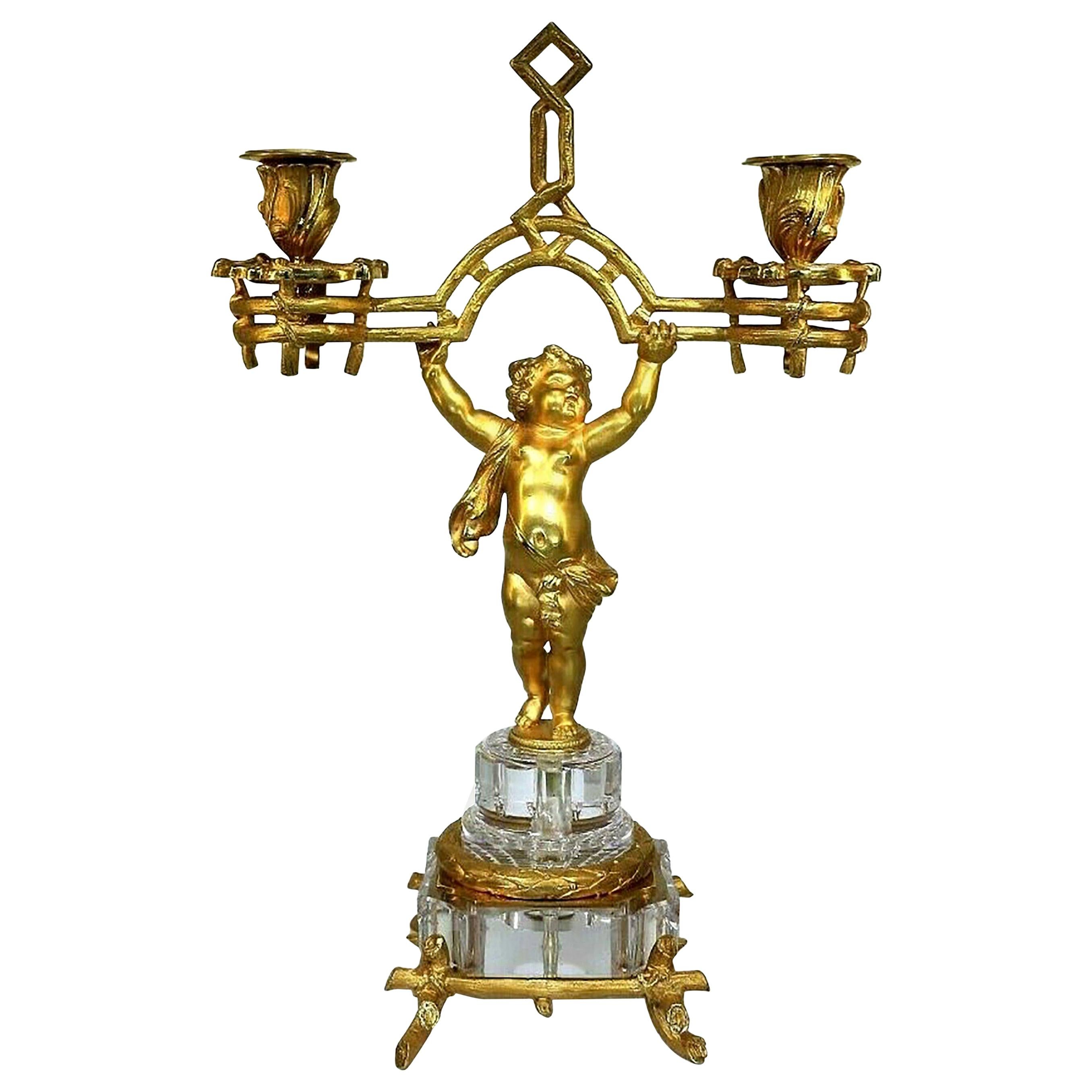 Baccarat bronze chandelier bronze, fire-gilded, partially polished. Elaborately cut crystal glass.
Two-armed shape, shaft as a standing putto on a glass base and plinth, this held with a knot-like and wreath-like mounting.

Baccarat and company