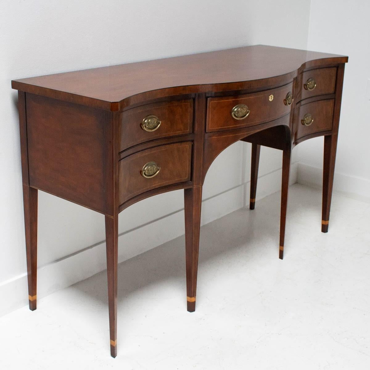 Classic mahogany sideboard made by the venerable Baker Furniture Company. It is part of their Historic Charleston Collection. Features a serpentine facade features a central drawer above an elliptical arched apron flanked by drawers for additional