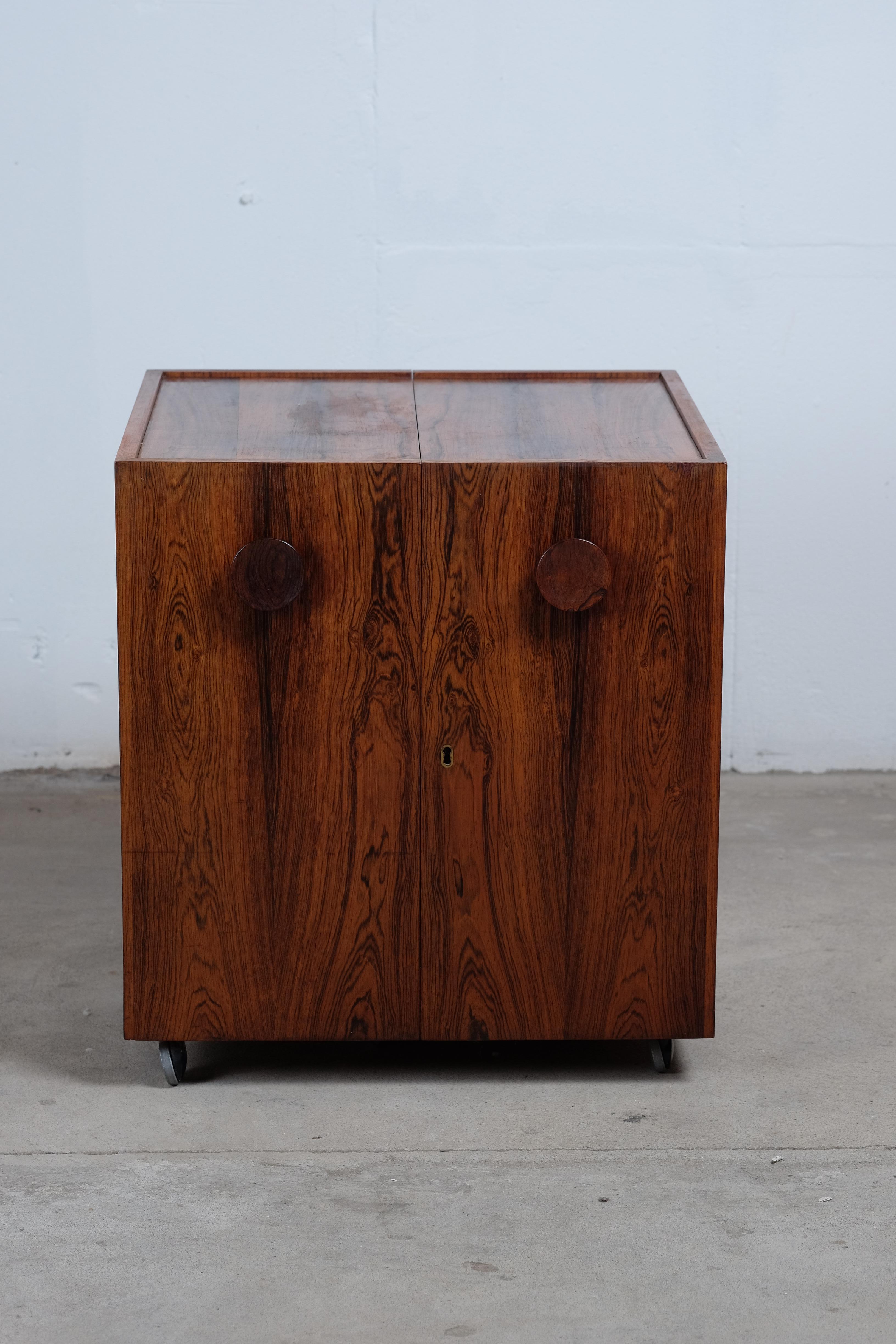 Square bar cabinet designed by Erik Buch, manufactured by Dyrlund around the 60s. Danish design.
Rosewood with brass details, two adjustable/removable linoleum trays and six metal wheels under. The lock doesn't work, but can be fixed by an
