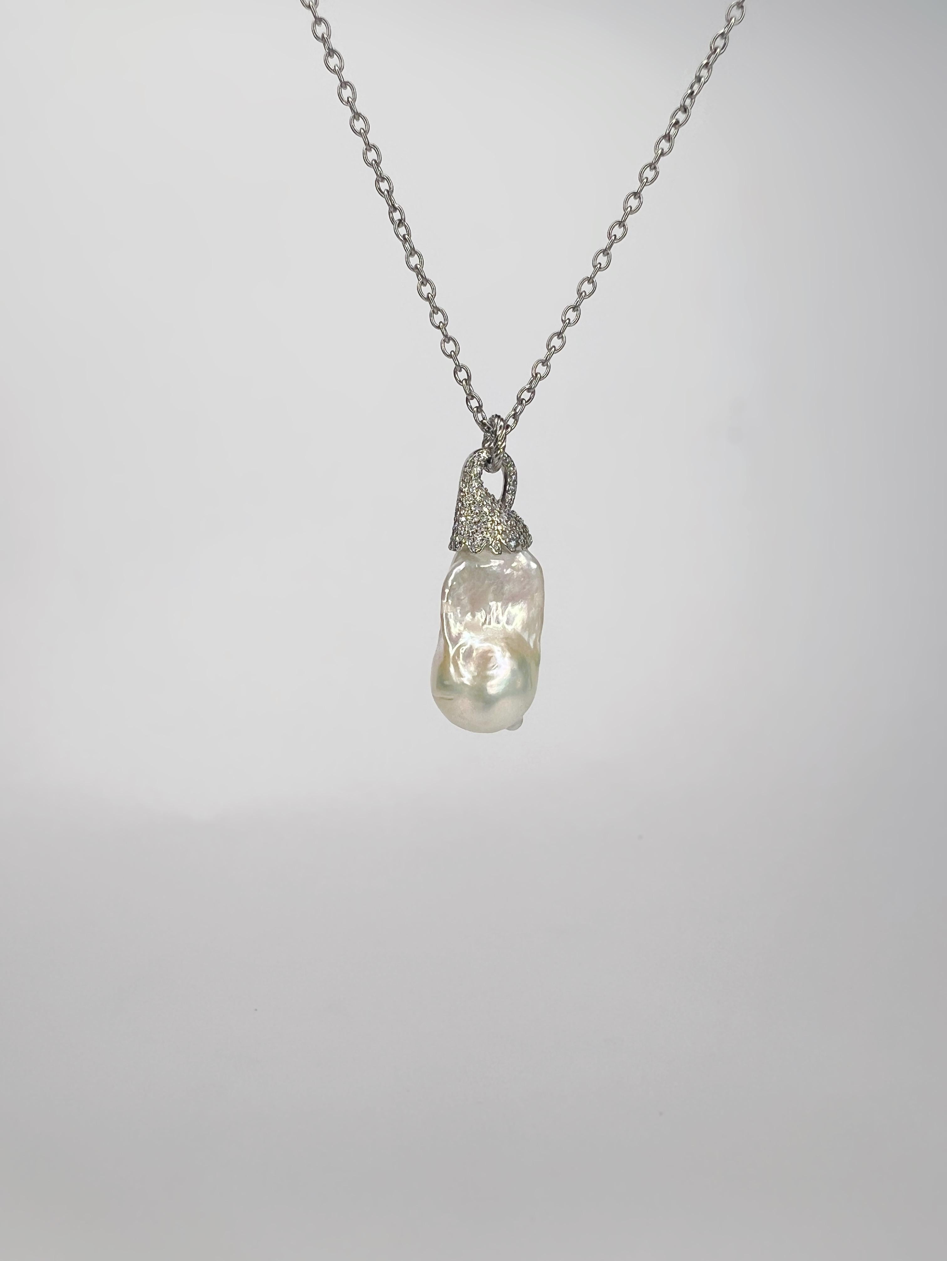 Questo elegante ciondolo cattura la bellezza senza tempo di una splendida perla barocca, graziosamente sospesa in un'intricata e scintillante cornice. La delicata struttura è ornata da scintillanti cristalli Swarovski, che creano un contrasto