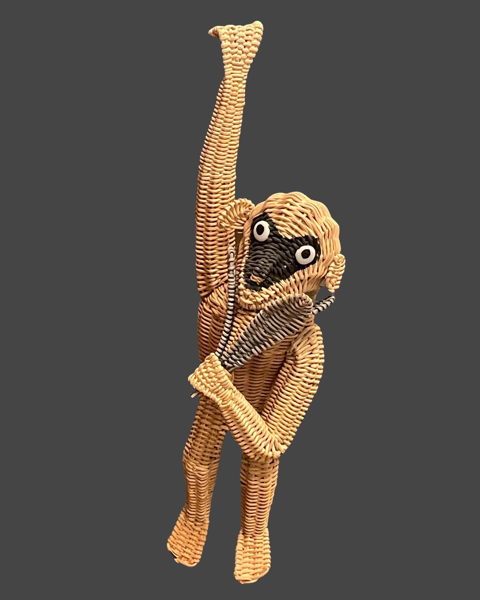 A large hanging wicker monkey holding a grouping of leaves. This cute brown monkey is created from wicker and features arms and legs which are bent so that they may hang from any spot. He has beaded eyes, a black face, and holds a bundle of green