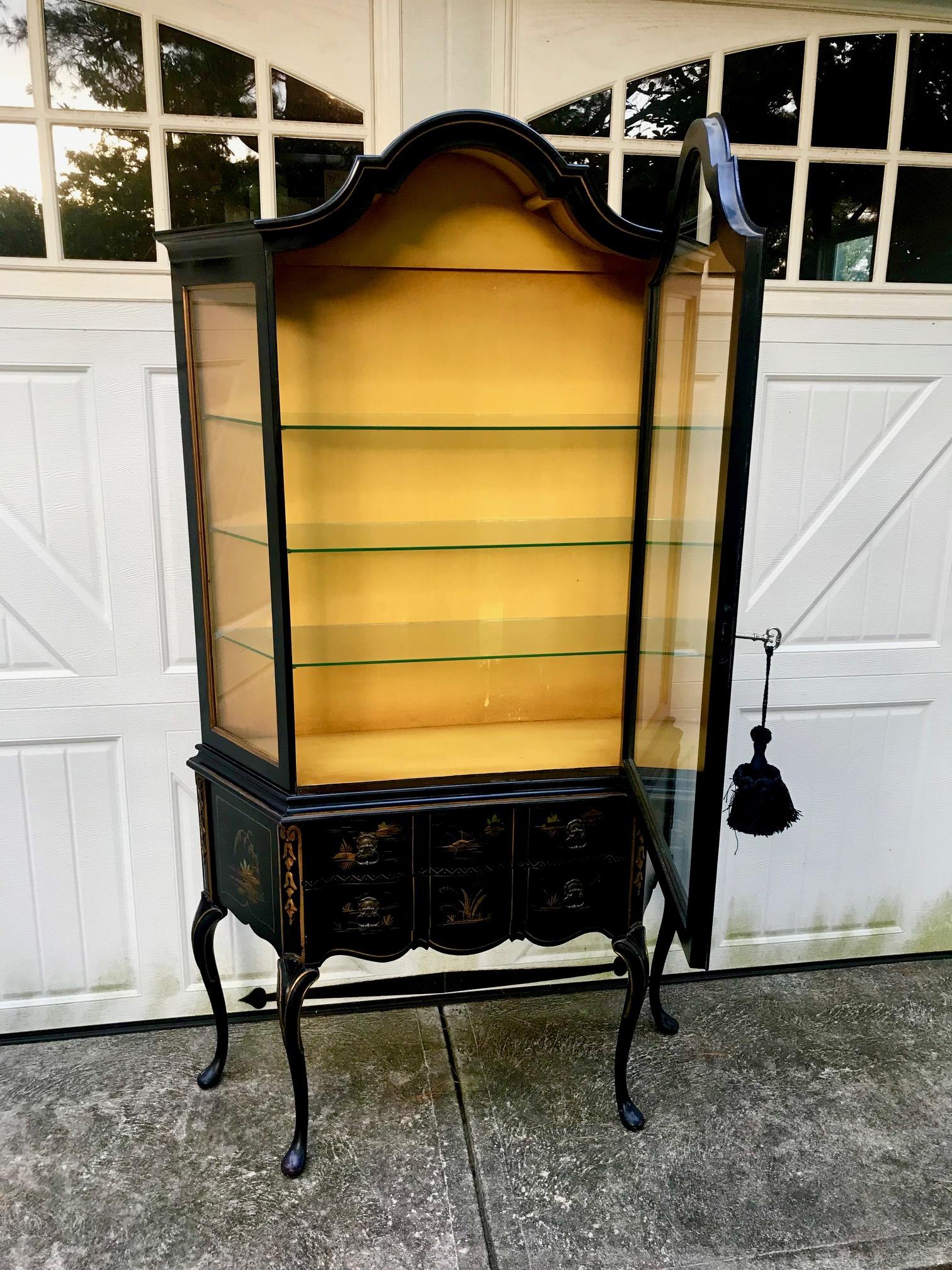 Luxurious elegant display cabinet having Chippendale style silhouette with curved top, 3 sided glass top, two drawers on the bottom and cabriole legs, beautifully decorated with figural gold against black chinoiserie embellishments. 3 interior