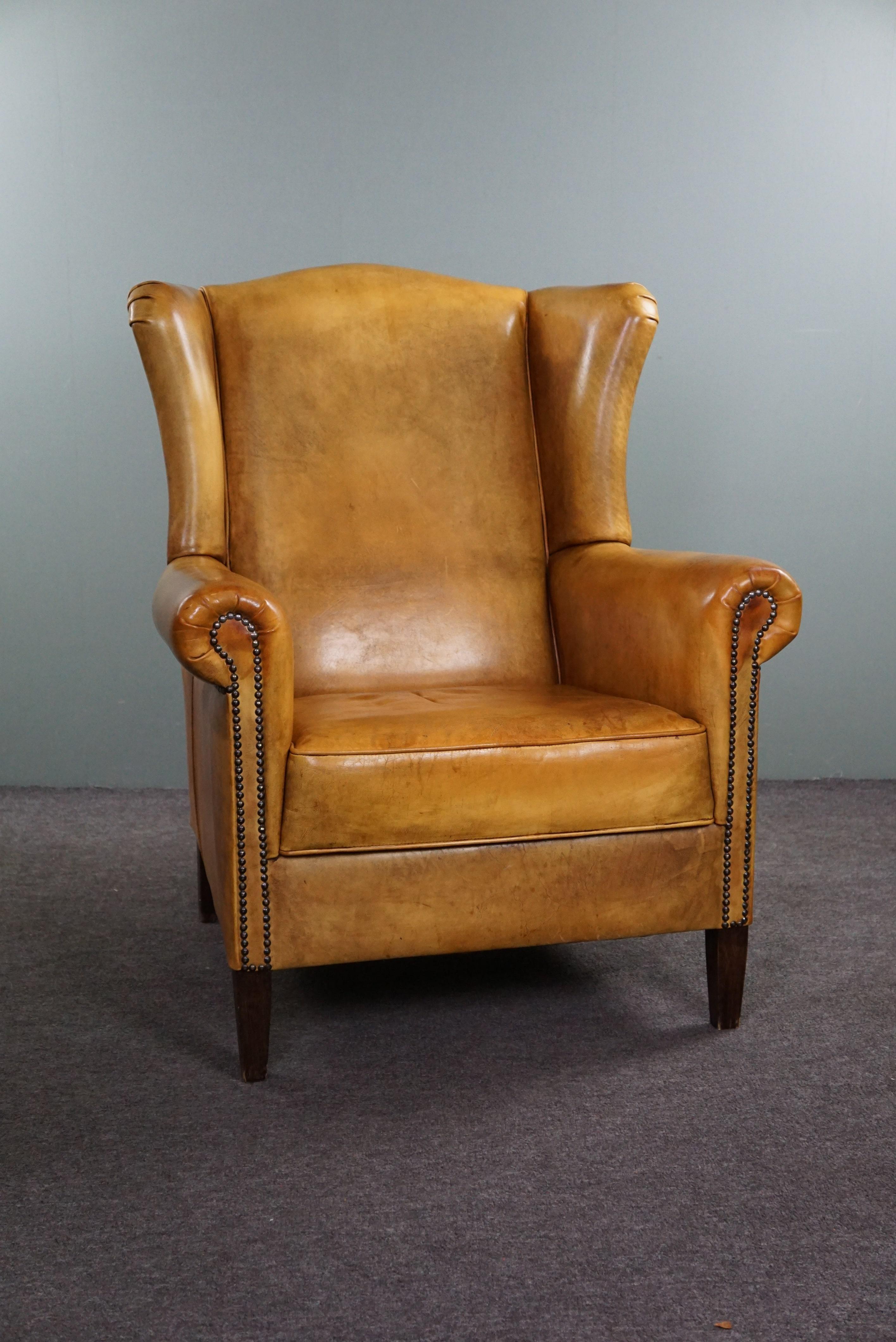 Offered is this warm-colored blonde wing chair finished with decorative nails.

This pearl has an unsurpassed expressive color and a beautiful patina. The armchair has beautiful divisions in the leather all around and is subtly finished with