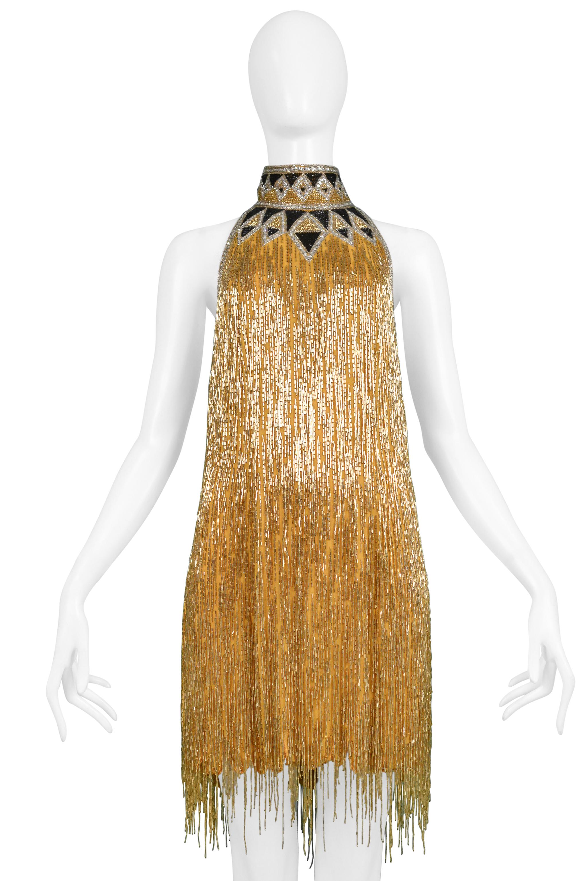 Resurrection Vintage se complace en presentar un impresionante vestido vintage de Bob Mackie con cuentas doradas y negras, cuello alto, espalda descubierta, cremallera central trasera y largo mini. El vestido tiene forro interior de seda. 

Bob