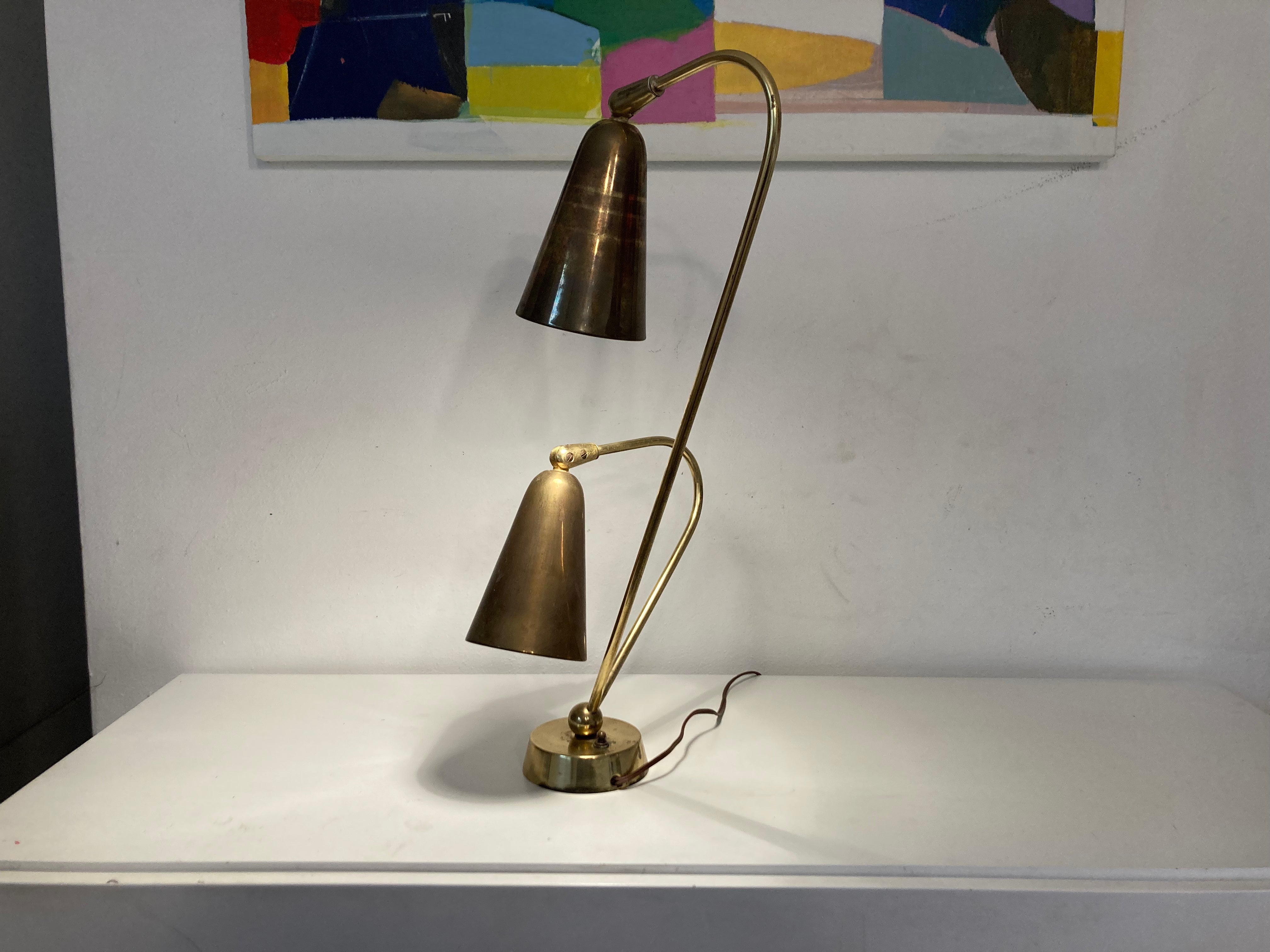 Beautiful Brass Table Lamp from the 1950s, two curved arms that emanate from a cylindrical base. At the end of each brass arm is a conical shade, great quality. 
The lights can be lit simultaneously or independently of one another via a three way