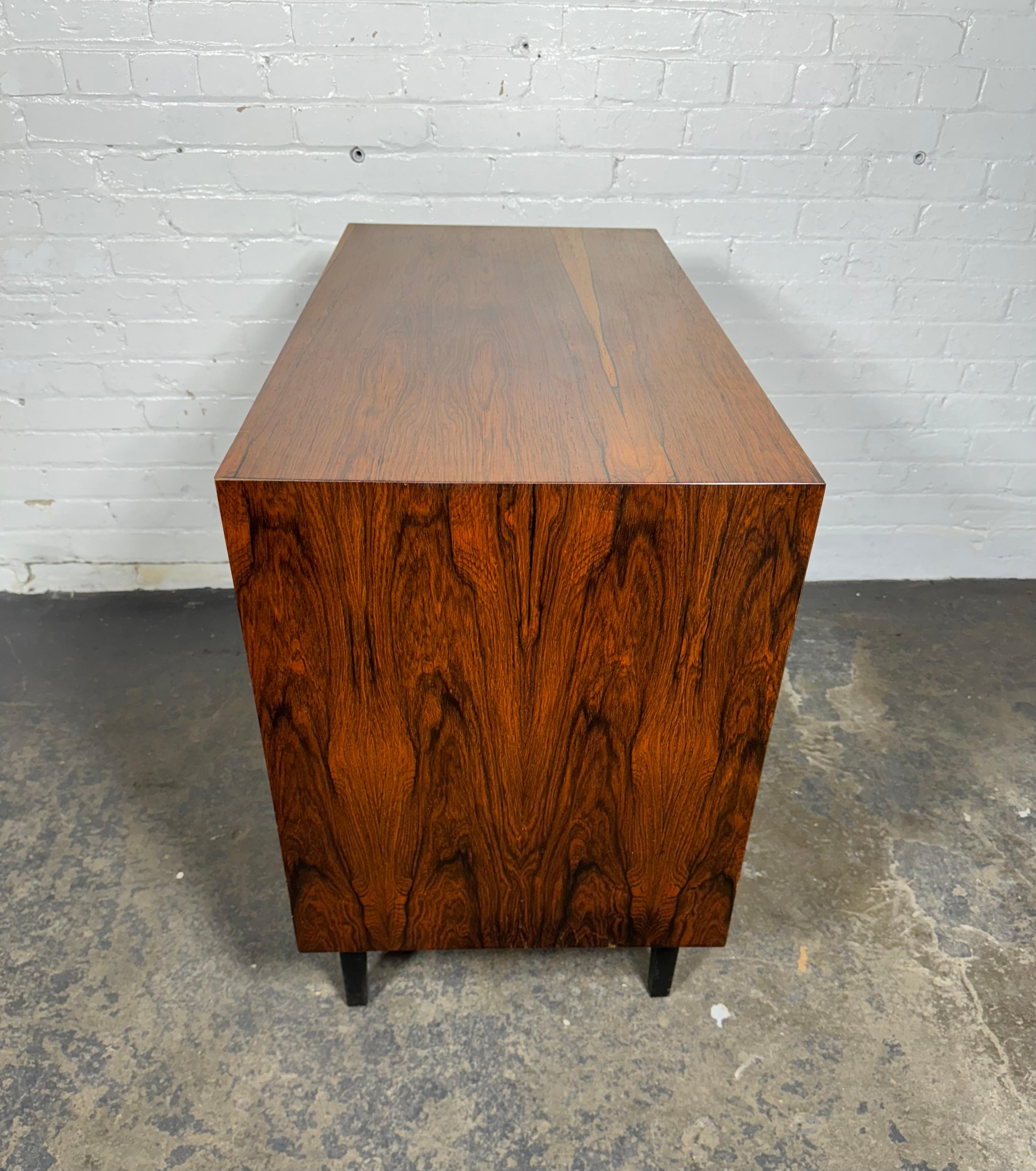 Classic Danish Modernist Rosewood cabinet with stunning book-matched doors revealing an interior of mahogany with adjustable shelf. Minimal design with mitered corners and unusual aluminum pulls. Raised on lacquered legs. Perfect as a bedside table,
