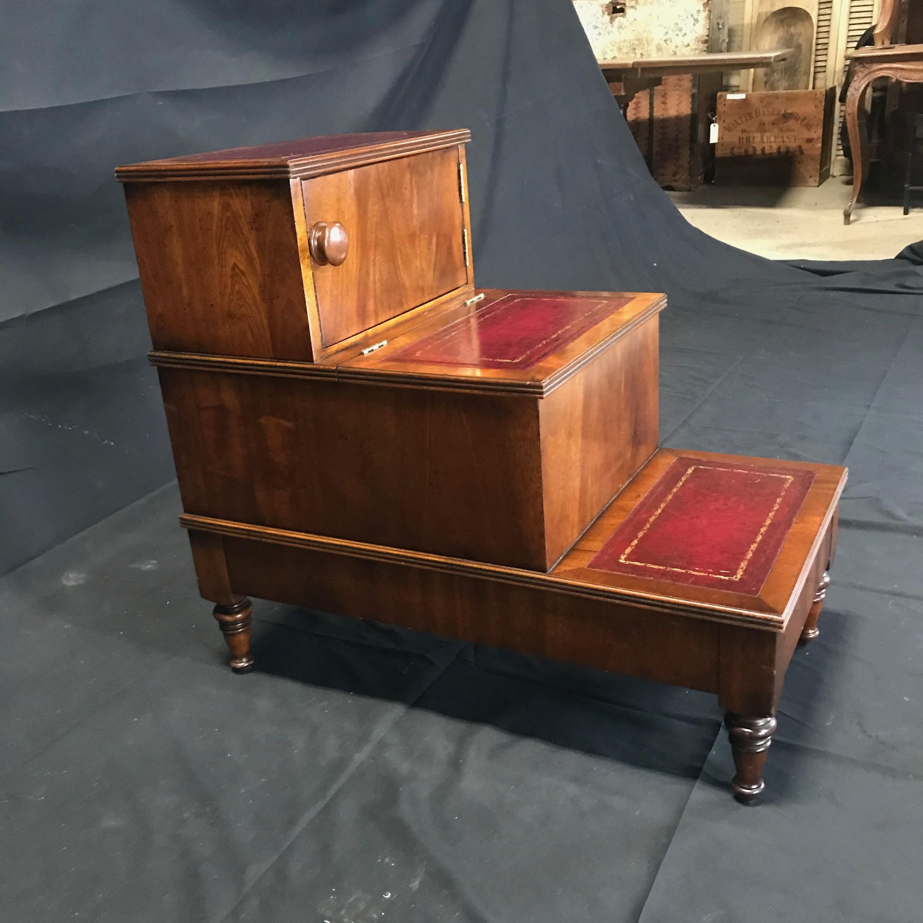 An unusually handsome set of mahogany library steps having a lovely burgundy tooled leather on the treads, ebonized inlaid design on front of steps and reeded detail on base and tops of steps. The piece includes a rare perk, having two storage