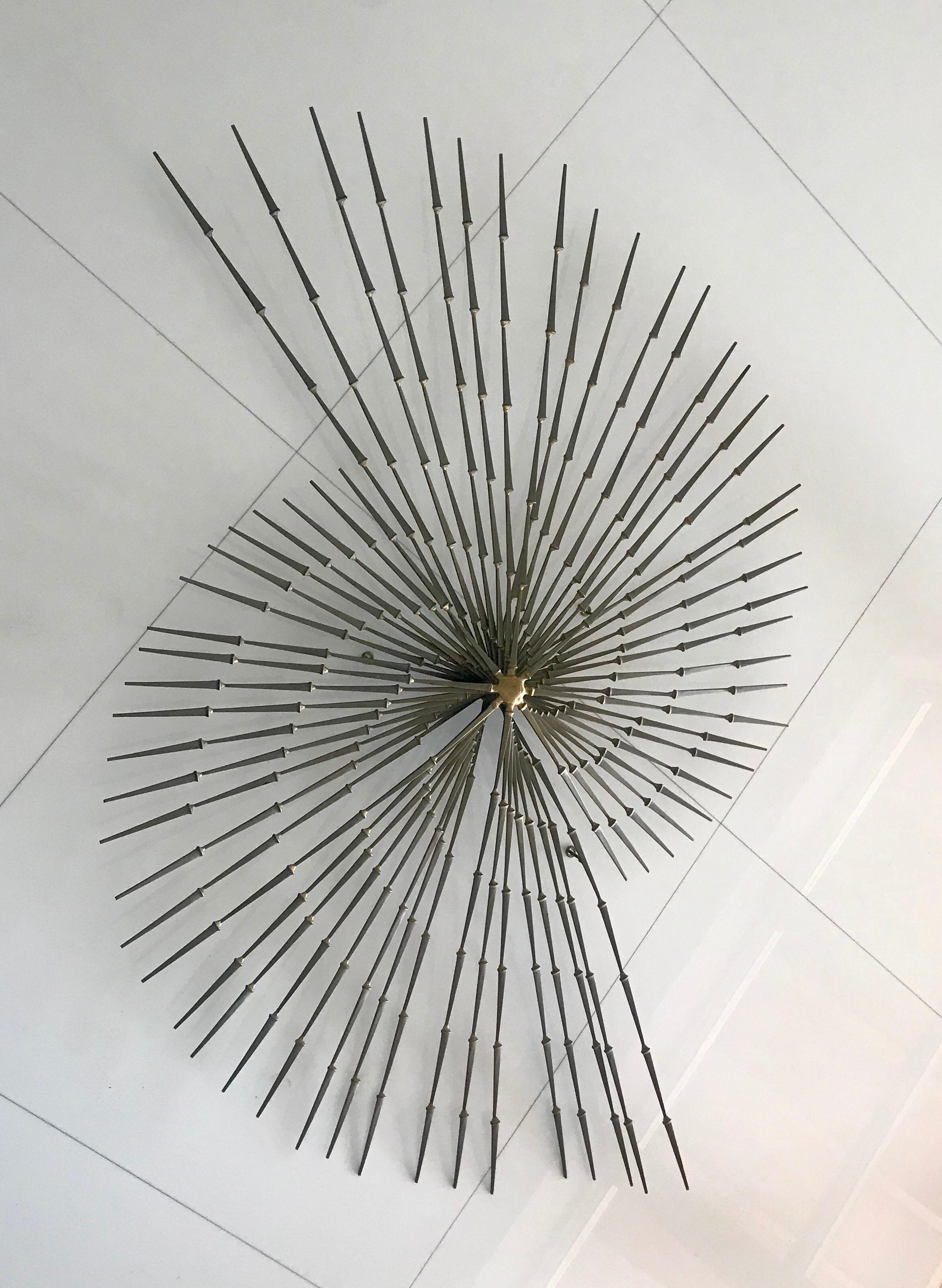 The blackened steel and brass form a dynamic complement to each other and the nails are tapered to form rays as they extend outwards. The pinwheel starburst reflects modern design, brutalism and neoclassical aesthetics.