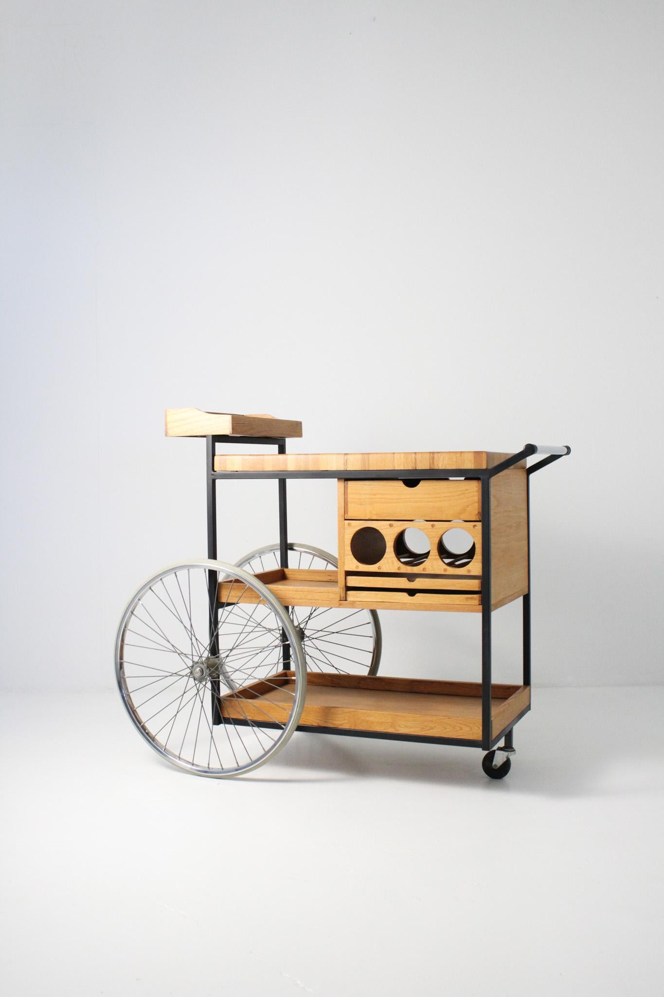 Extraordinary oak and mahogany three wheel serving cart by Arthur Umanoff. Black lacquered iron frame, large bicycle style wheels and a single pivoting wheel. Butcher block top with center polished aluminum textured disc. Three wine bottle holder