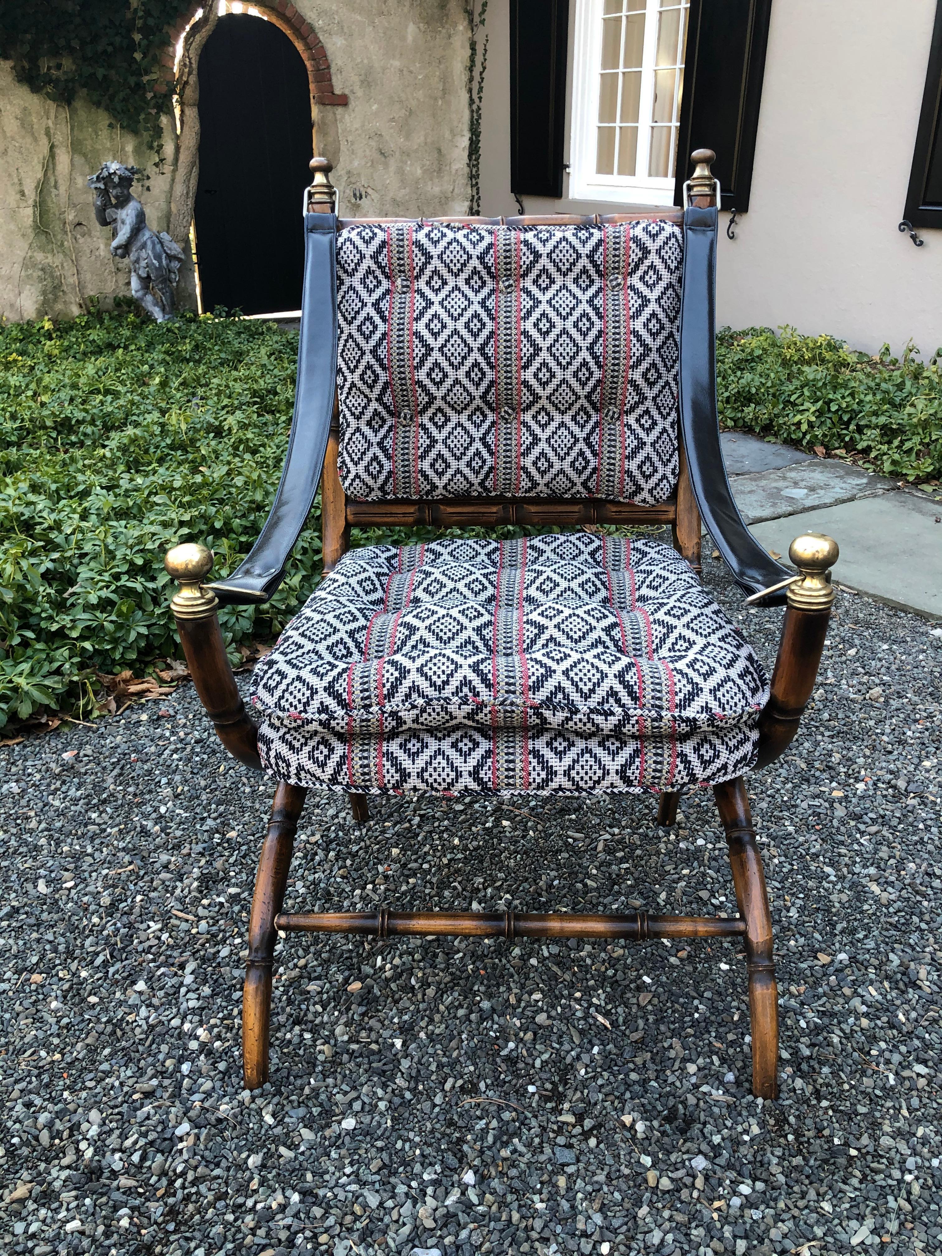 Fascinating campaign safari chair in a faux bamboo wood. The seat and back are cane with newly upholstered tufted cushions. The cushions are fixed to the chair with buttons. Leather straps serve as the arms and are attached with brass hardware and