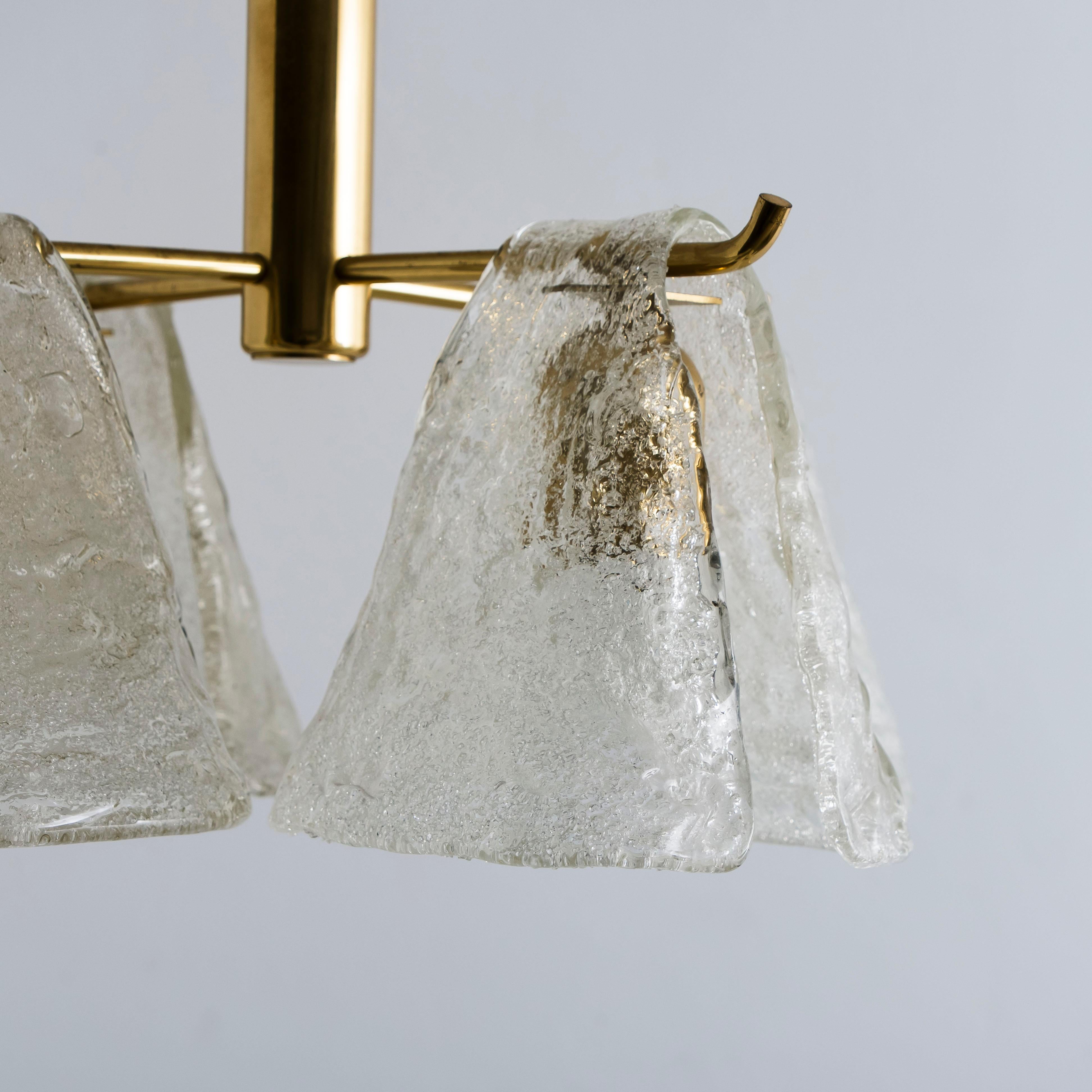 Dieser Kronleuchter besteht aus einer Messingstruktur, über die sich vier Lampenschirme aus geblasenem Glas zu ergießen scheinen. Leuchtet wunderschön. 

Handgeblasenes Schmelzglas, hergestellt aus strukturiertem Glas. Hat eine sehr schöne