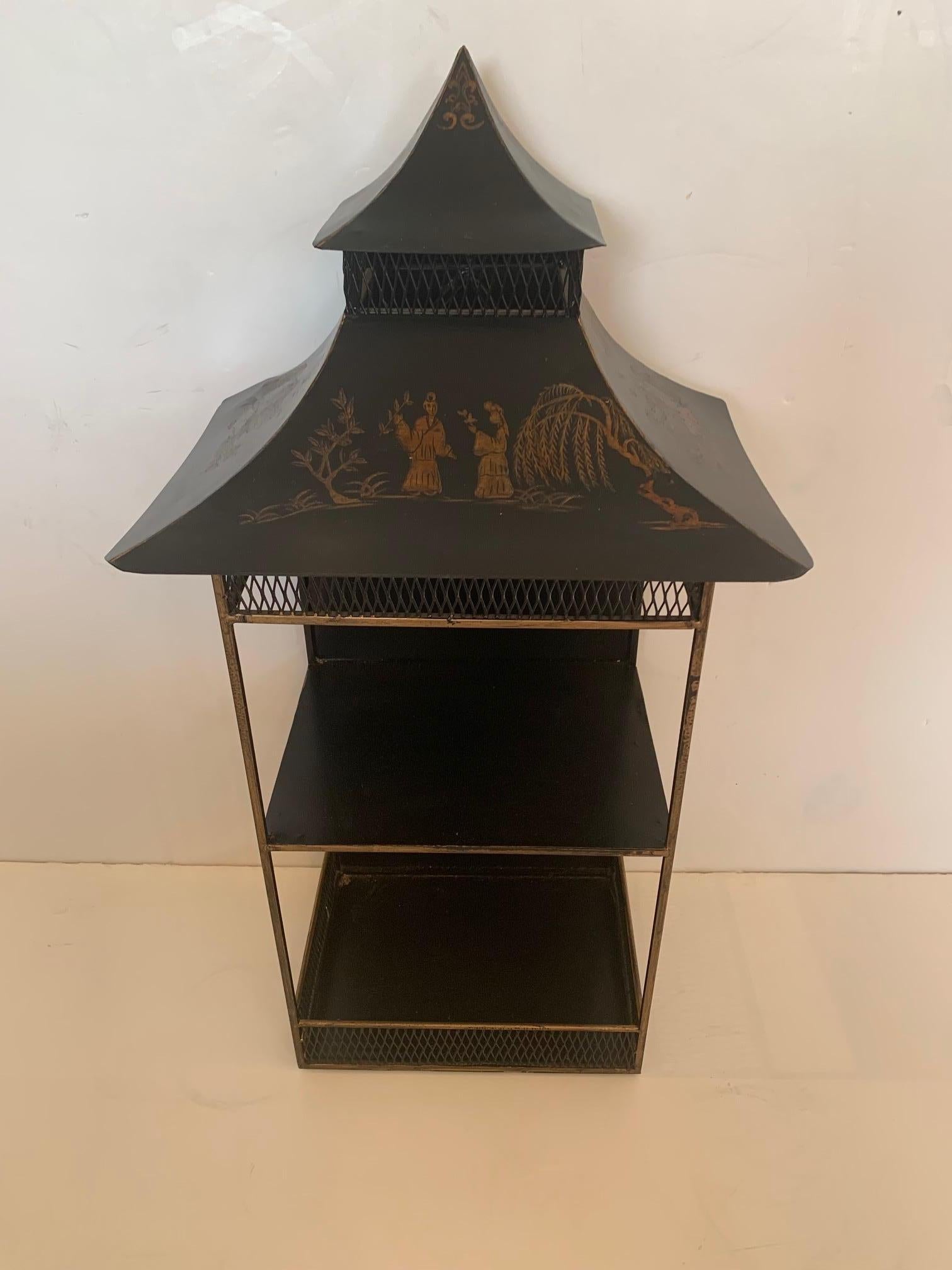 Striking pagoda shaped chinoiserie painted tole and iron hanging wall etagere in black and gold. Two shelves and wonderful silhouette.