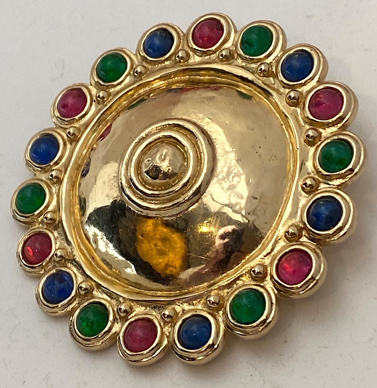 A beautiful and large Christian Dior medallion brooch in the Etruscan style. The pin is lightly domed in the center with a polished martele' texture and bordered with red, green and blue glass cabochons along the edge. The gold plate is shiny and in