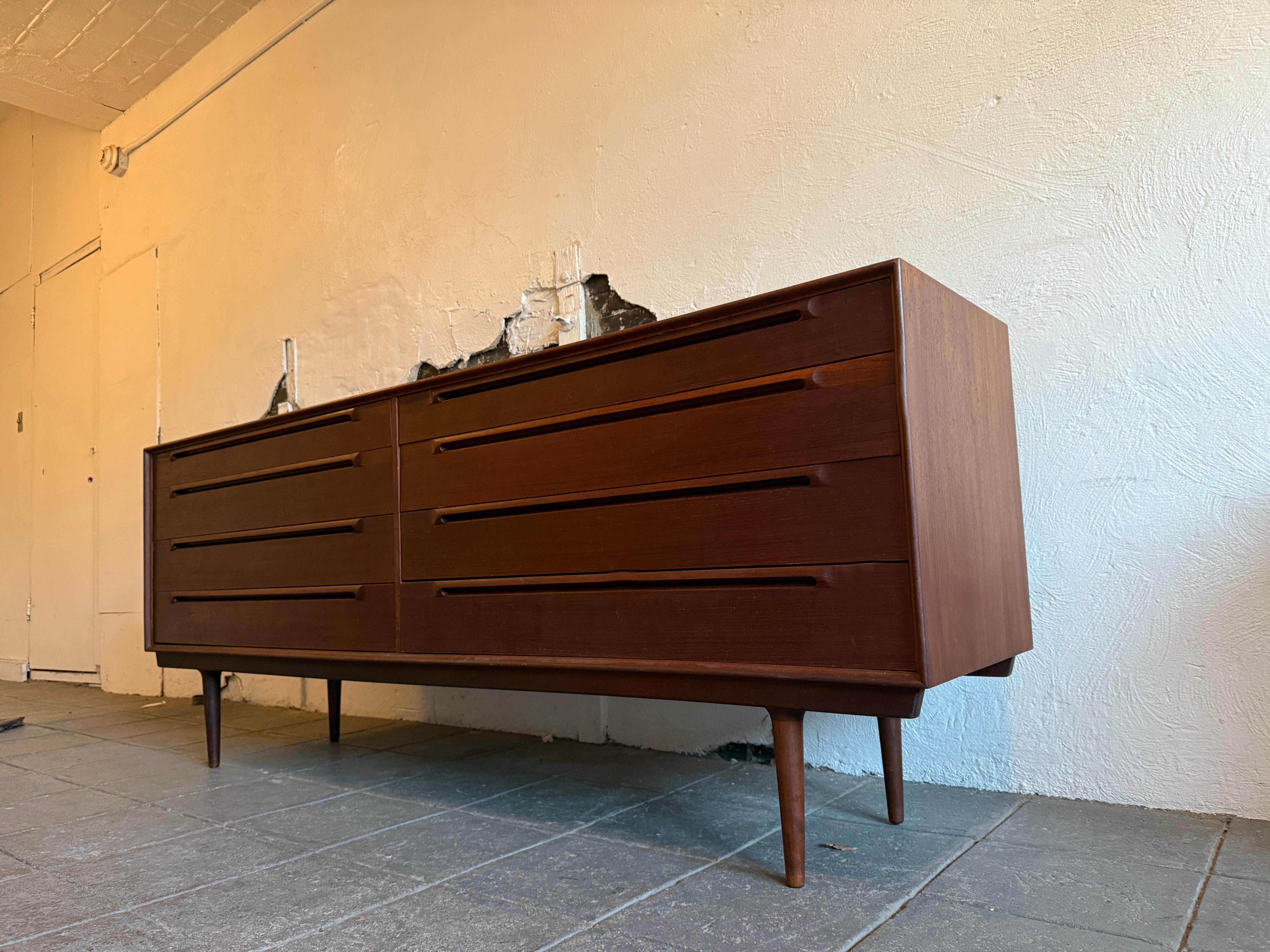 Cómoda danesa moderna Sven Ellekaer larga y baja de 8 cajones de teca. Asas talladas muy bonitas con grandes líneas. Cómoda muy larga de 8 cajones que se asienta sobre 4 patas cónicas de teca maciza. Gran Scandinavian Woodworks. Los (2) cajones