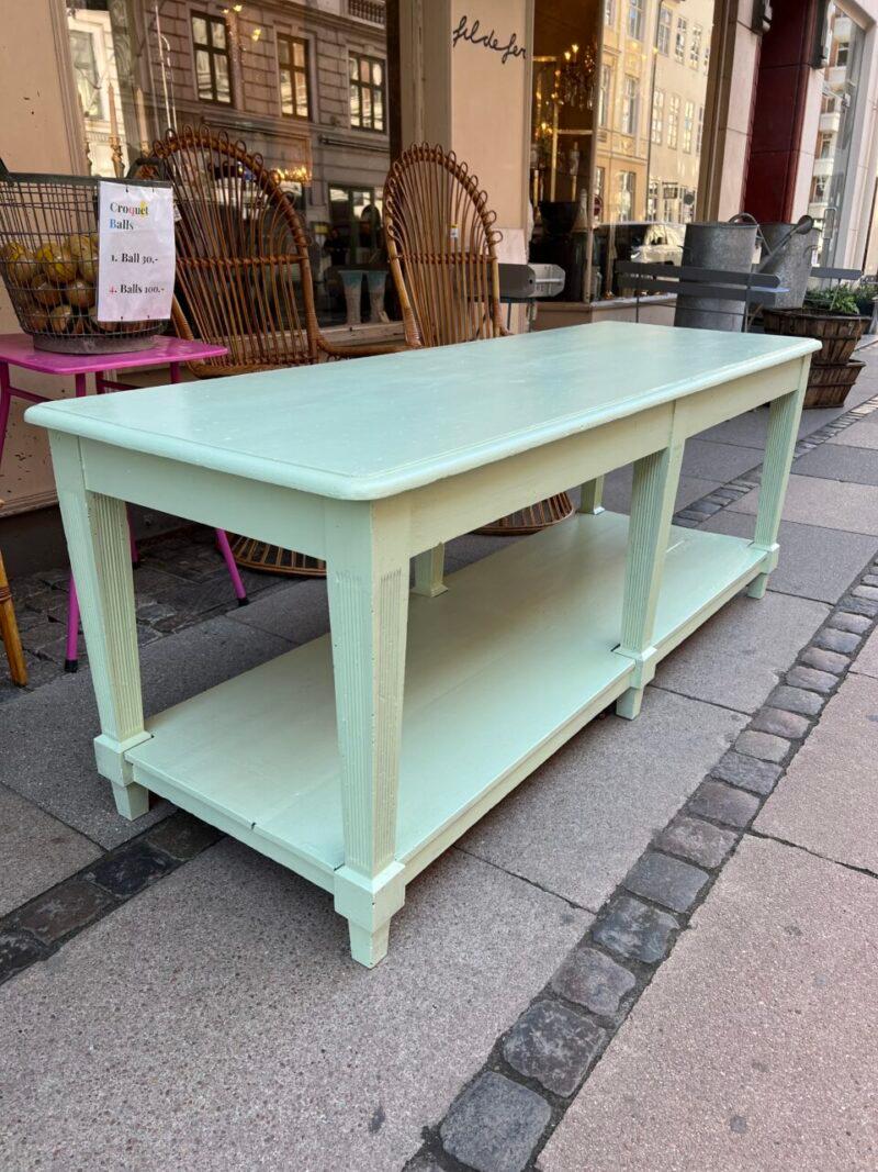 Handsome French console table from around 1900, painted a fresh green and with beautiful patina.

Originally part of a boutique’s inventory, where you could store fabric rolls/textiles on the shelf under the table top and on which to take metre